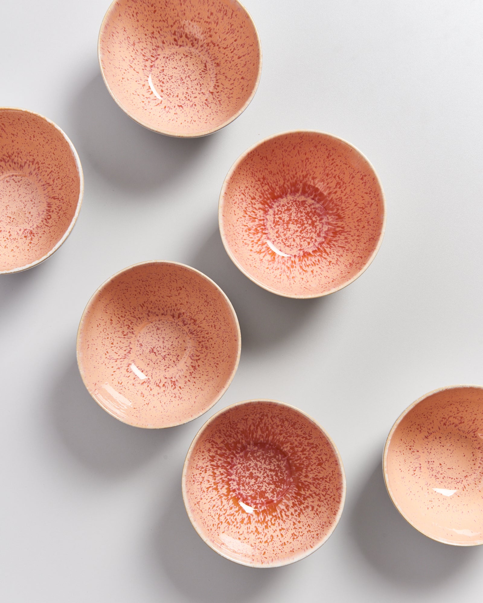 Sechs rosafarbene Schalen mit gesprenkeltem Muster auf einer hellen Oberfläche.