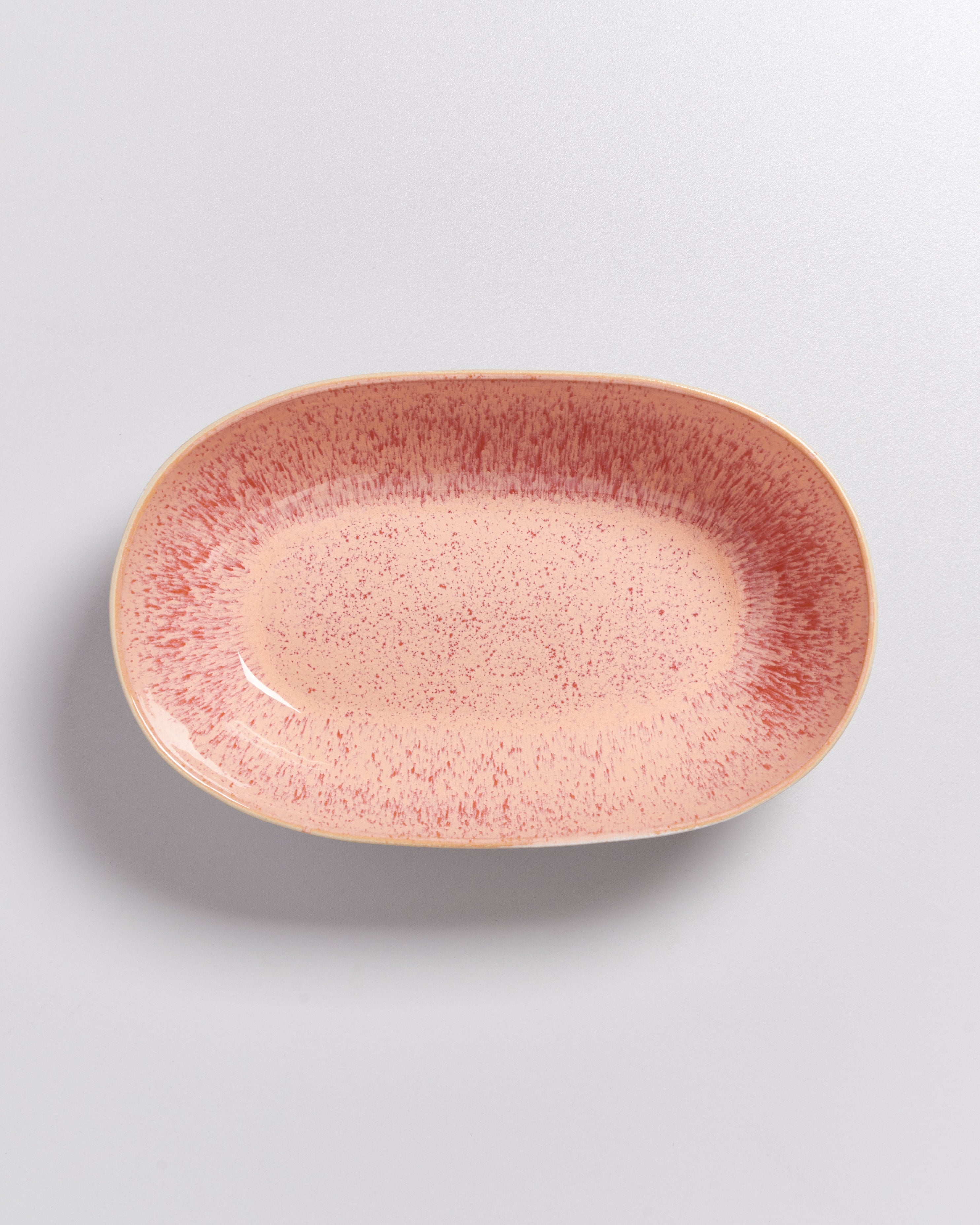 Ovaler, rosafarbener Teller mit roten Sprenkeln auf einer grauen Oberfläche.