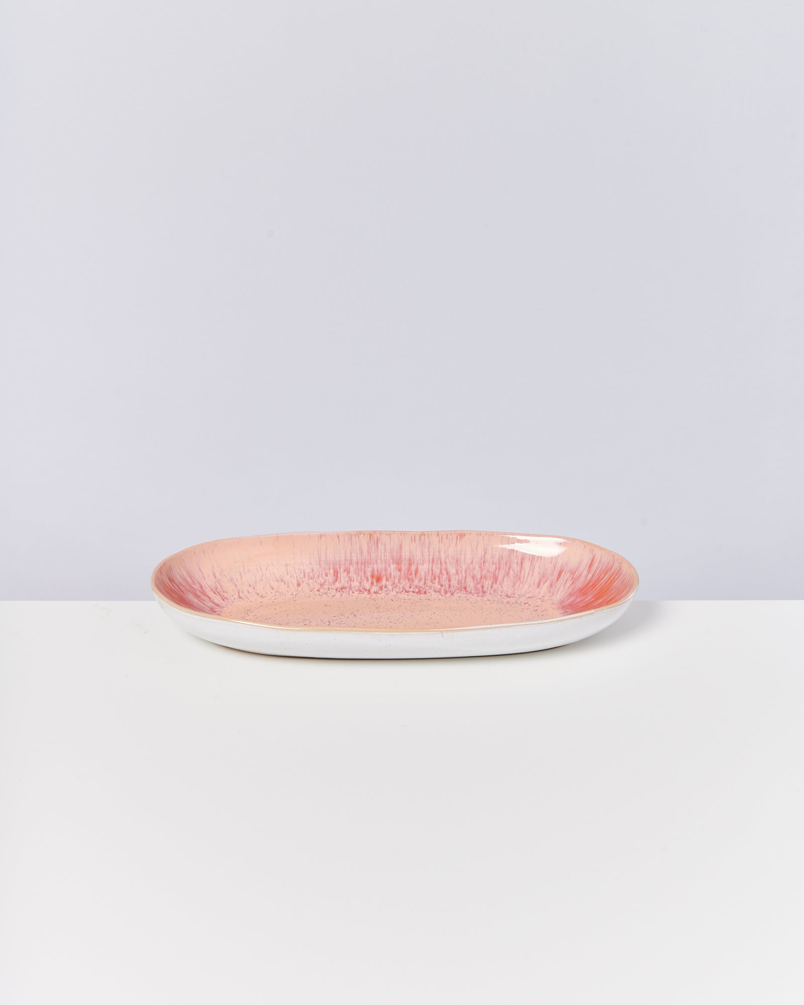 Länglicher Teller mit rosafarbenem und strukturiertem Muster auf weißem Hintergrund.