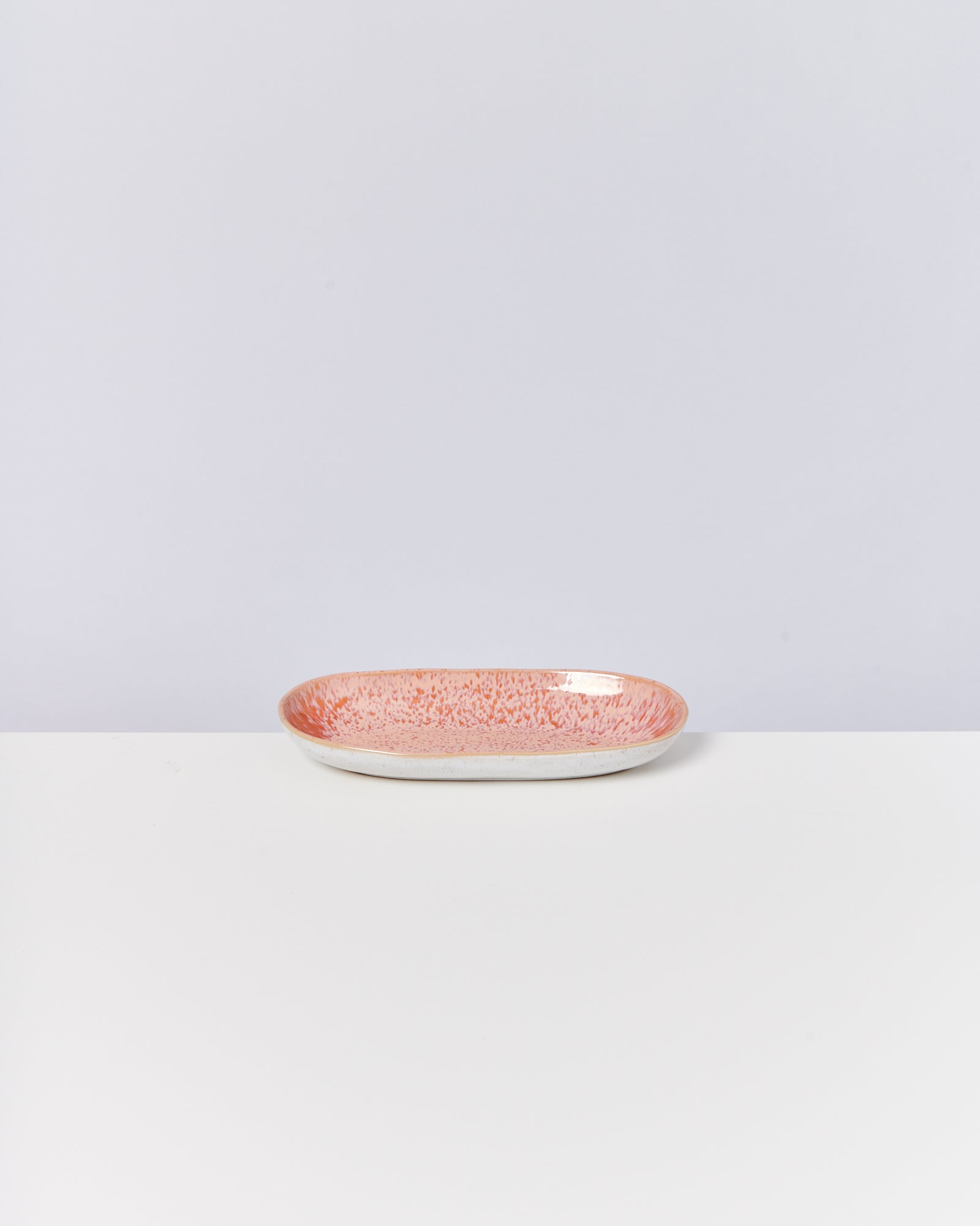 Ovaler Teller mit rot-weißem punktiertem Muster, auf einem weißen Untergrund vor grauem Hintergrund.