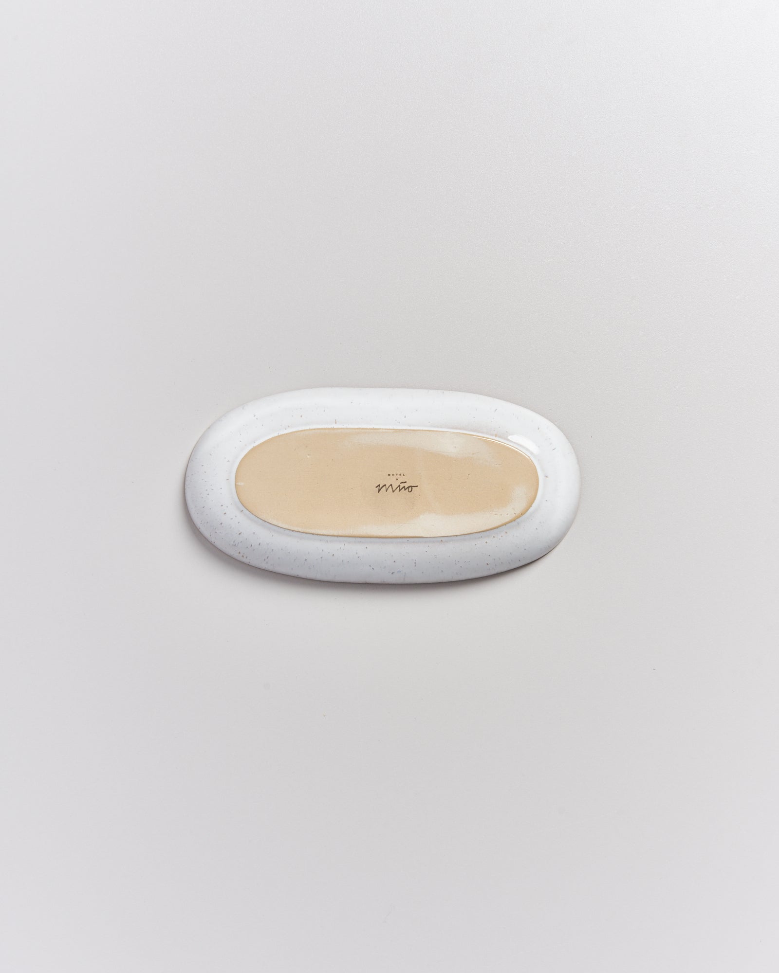 Ovale, weiß-graue Seifenschale auf einer weißen Oberfläche, von oben betrachtet.