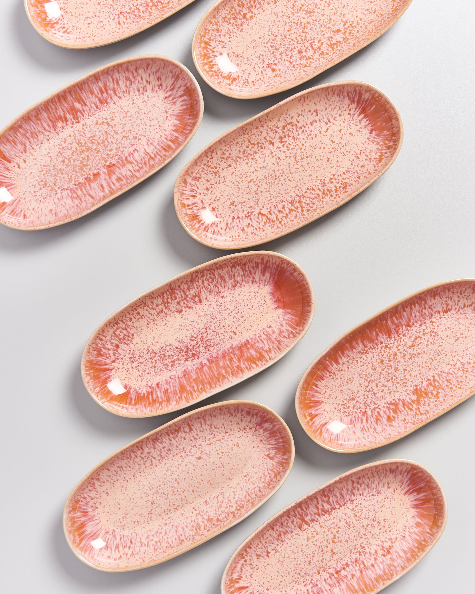 Acht ovale Teller mit rosa Sprenkeln auf weißem Hintergrund.