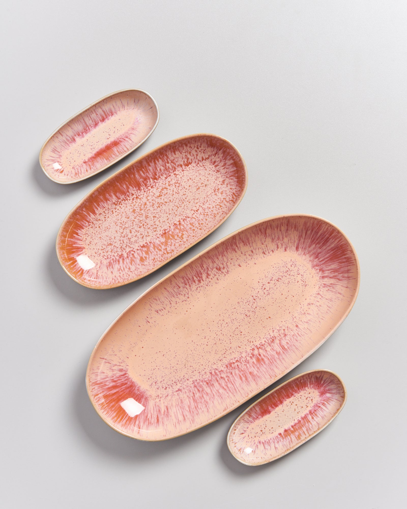 Vier ovale Teller in verschiedenen Größen mit einem rosafarbenen Sprenkelmuster auf hellem Hintergrund.