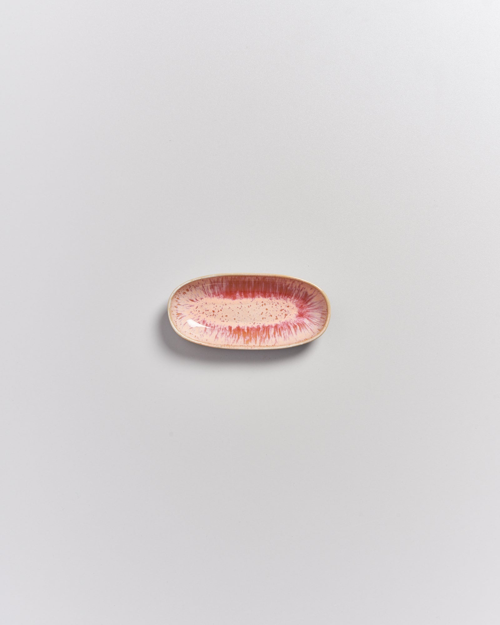 Kleiner, ovaler Teller mit rosa und roten Sprenkeln auf hellem Hintergrund.
