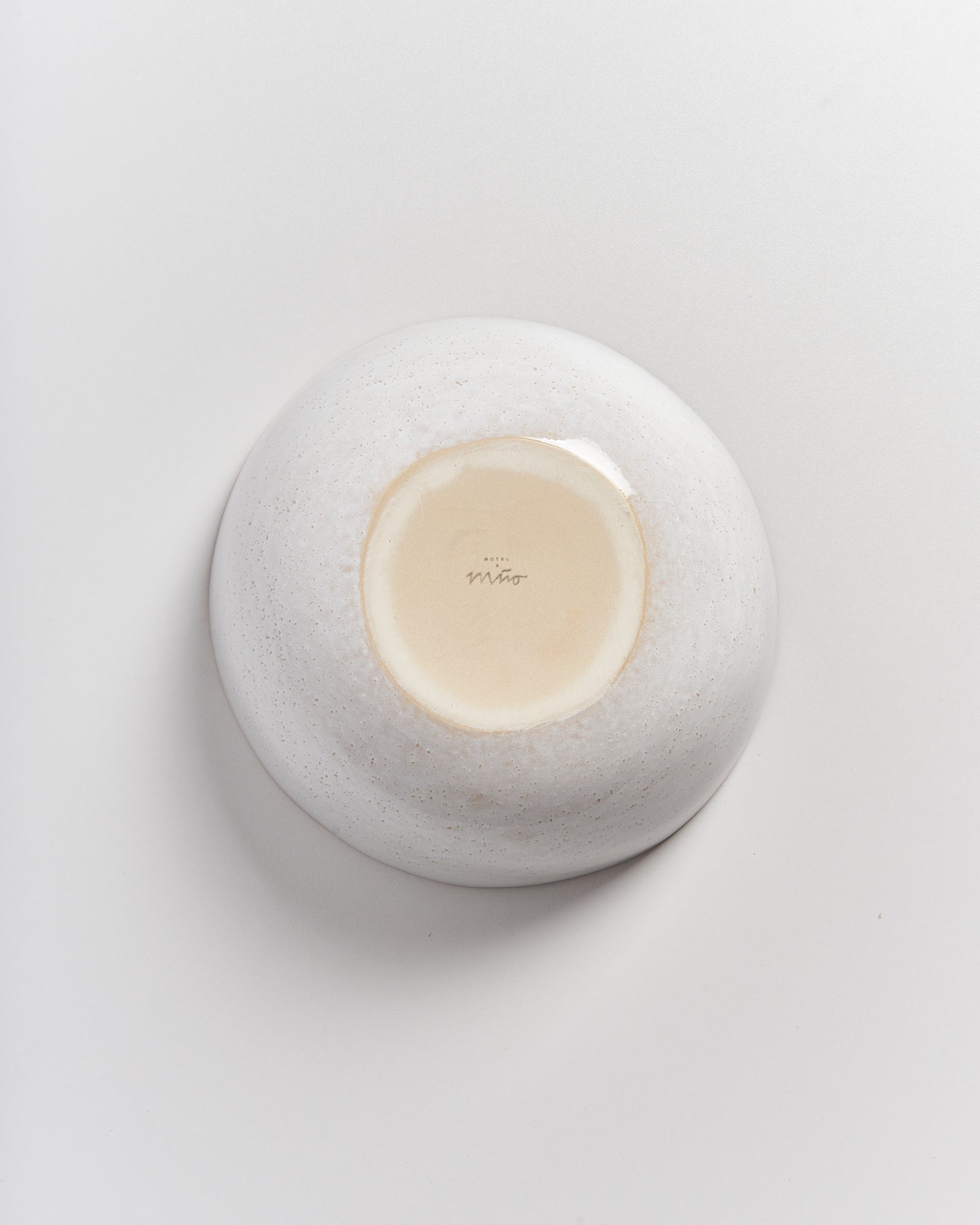 Unterseite einer weiß getupften, runden Keramikschale mit einem beigen Boden auf einer grauen Oberfläche.