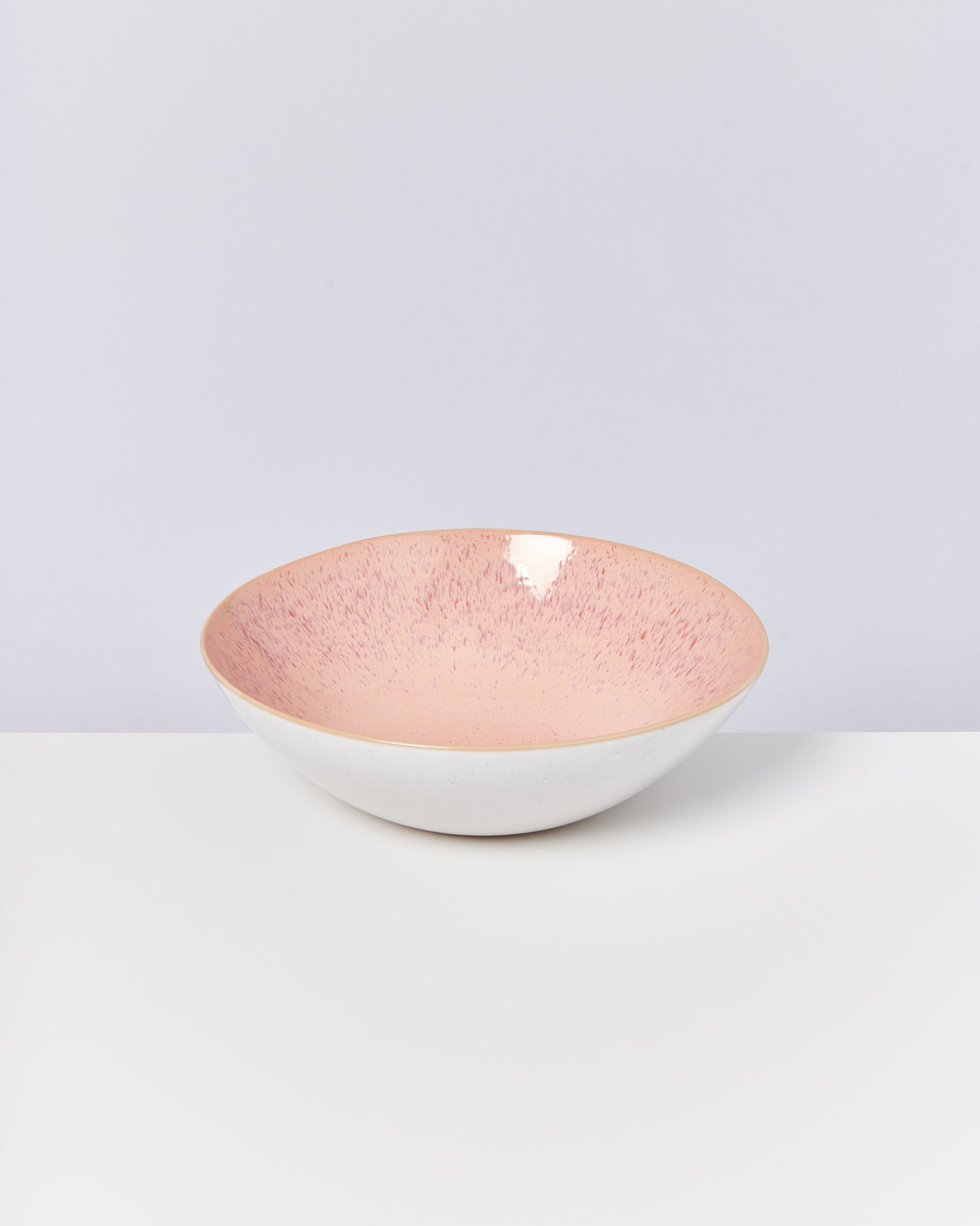Rosa-weiß melierte Schale mit glänzender Oberfläche auf einem weißen Tisch vor einem grauen Hintergrund.