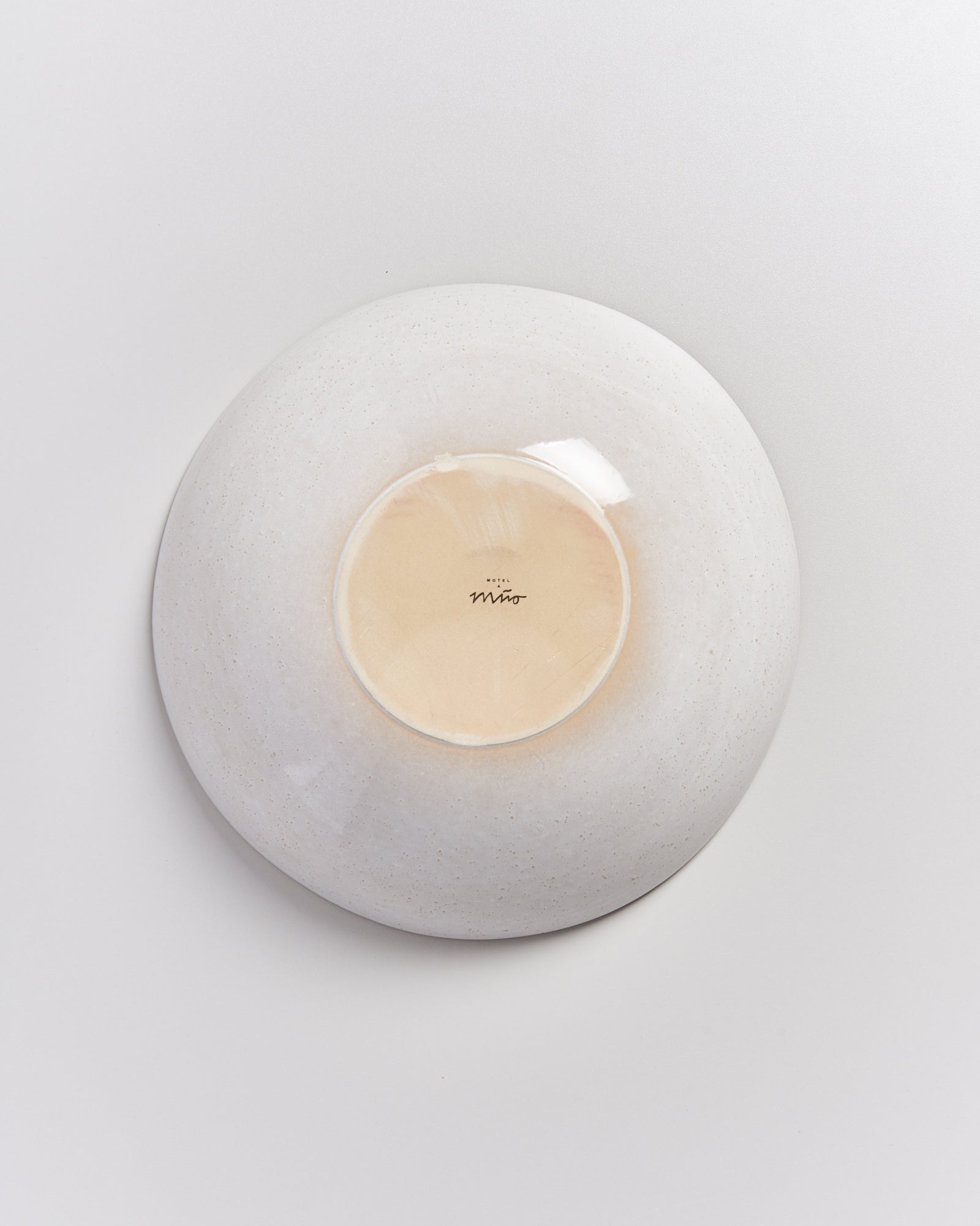 Eine umgedrehte, cremefarbene Keramikschale mit glatter Oberfläche und einem kleinen Logo auf dem Boden.