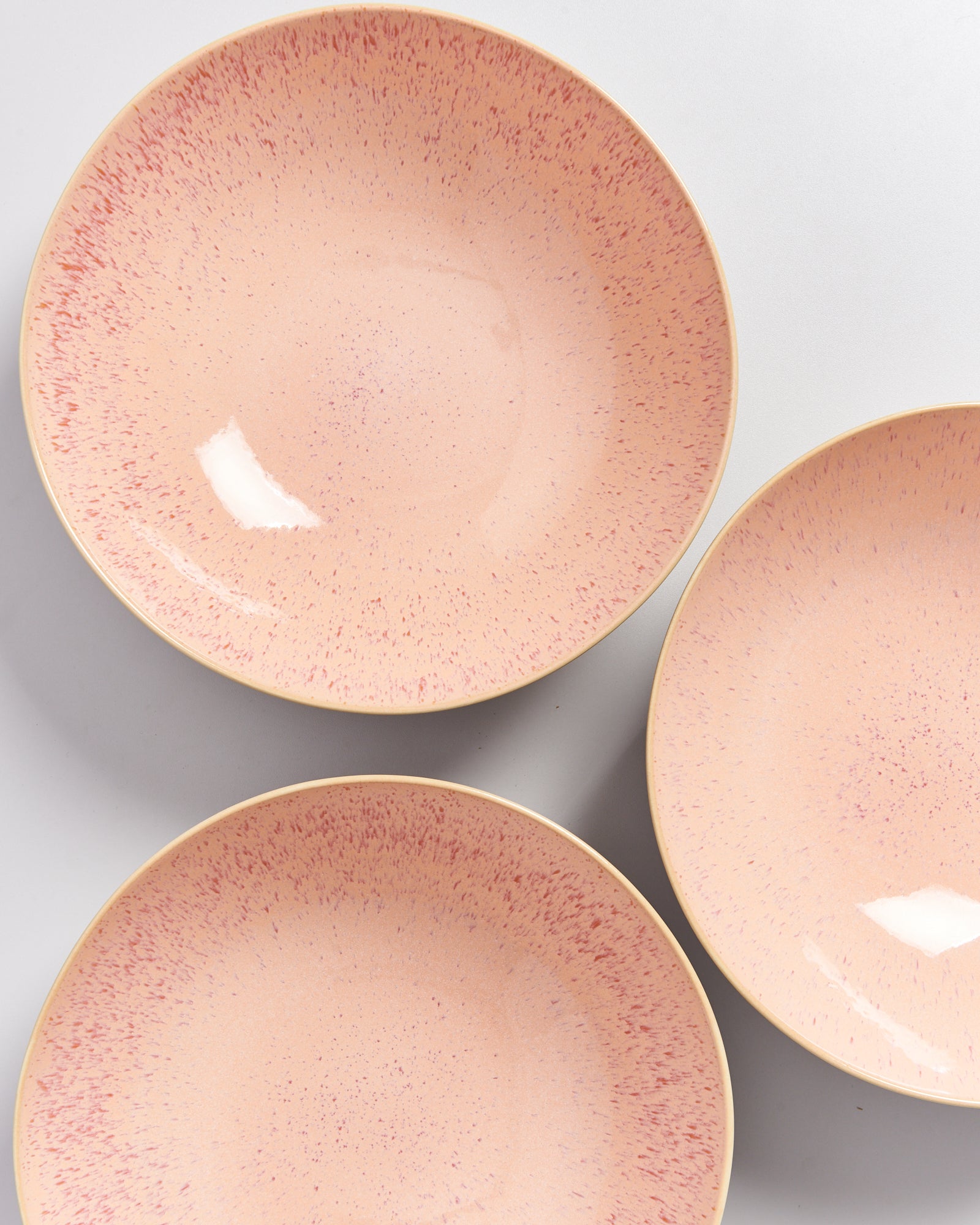 Drei beige Teller mit rosa gesprenkeltem Muster auf hellem Hintergrund.