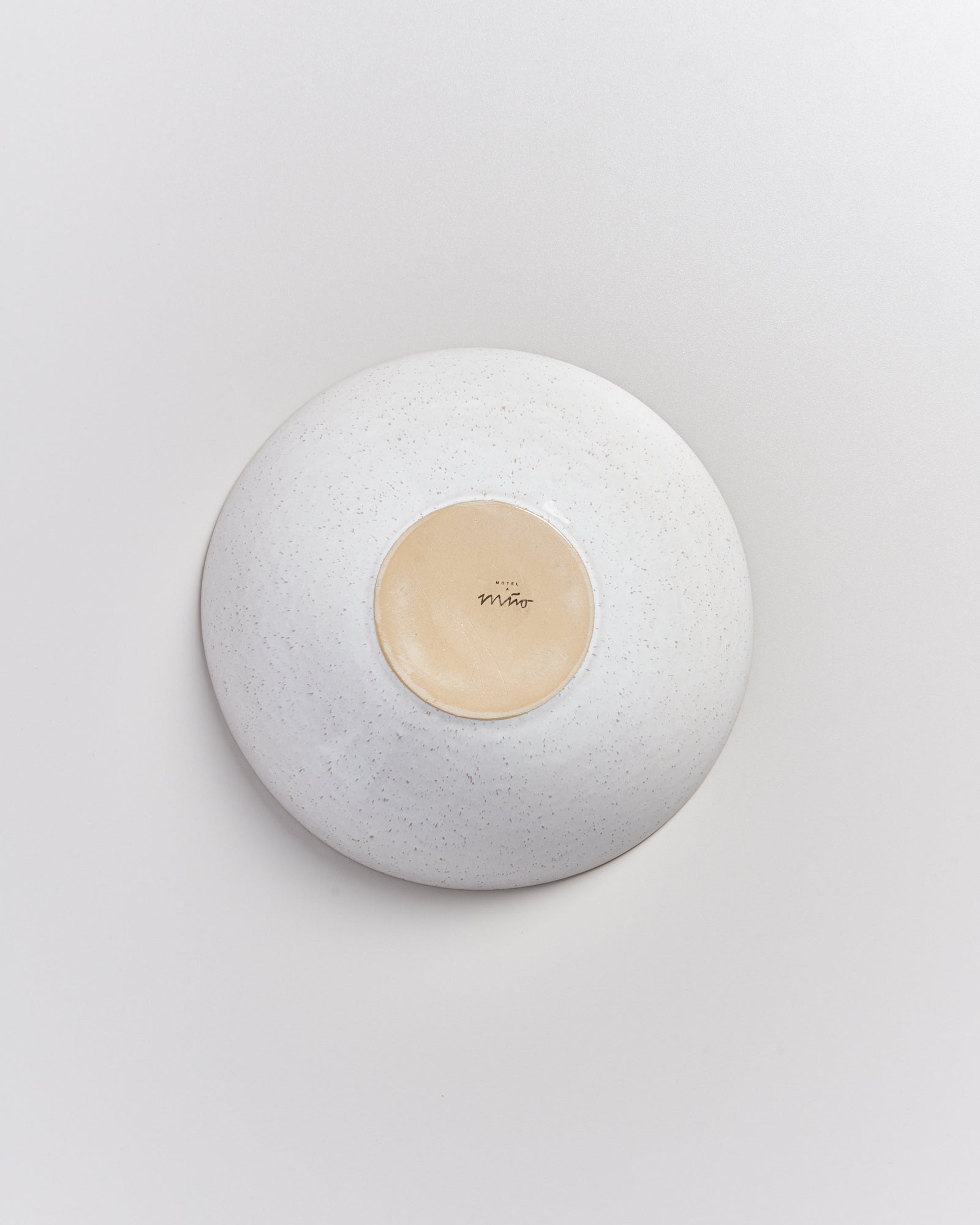 Eine weiße, umgedrehte Schale mit beigefarbenem Bodenmuster auf weißem Hintergrund.