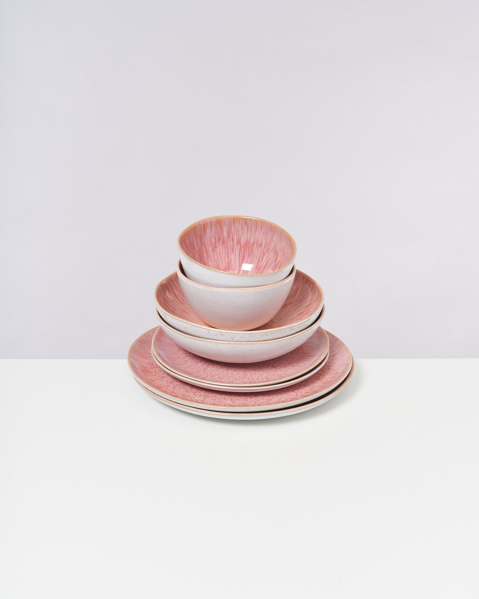 Ein Stapel rosa-weißer Keramikteller und -schalen auf einem weißen Tisch.