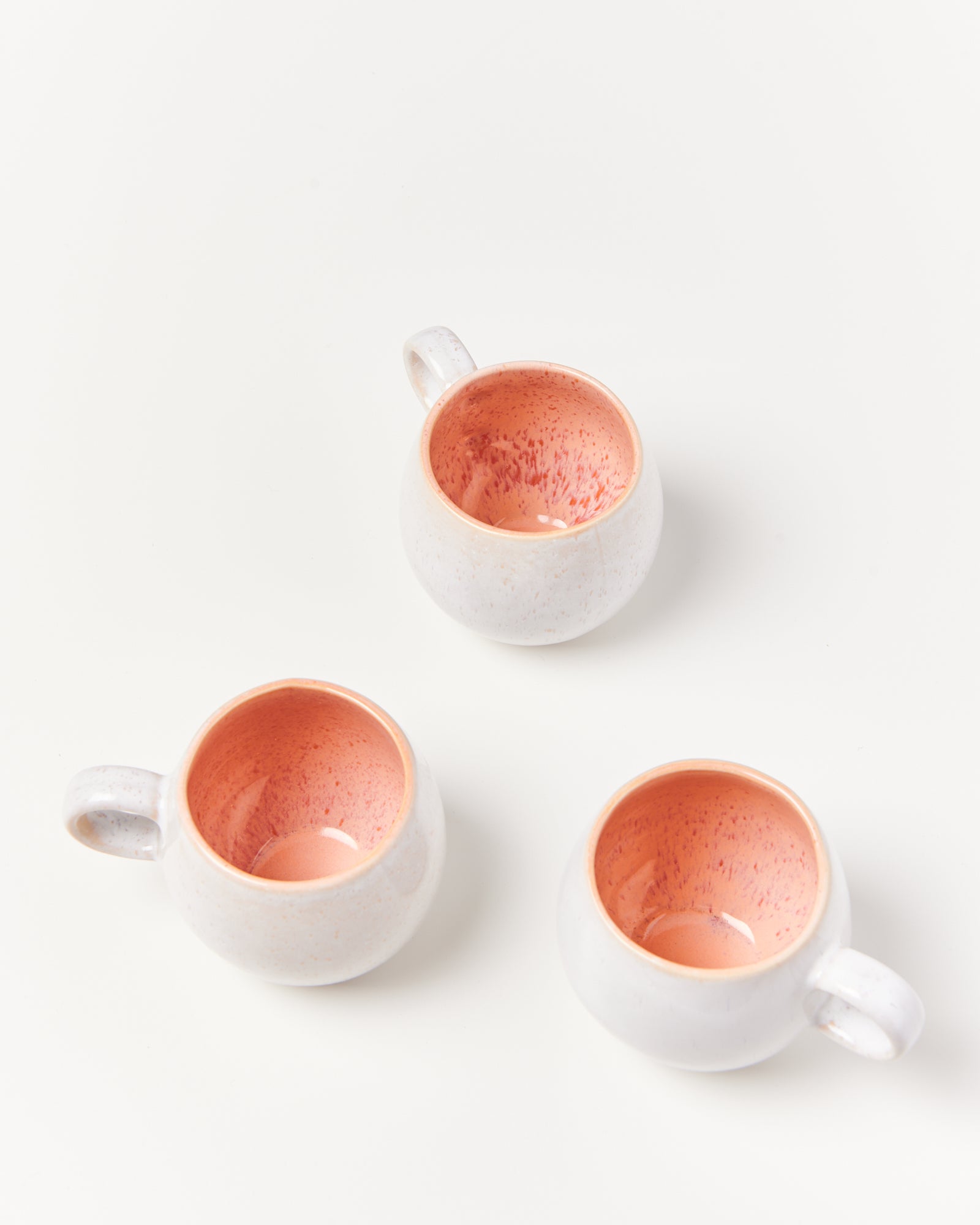 Drei weiße Keramiktassen mit rosa Innenseite auf weißem Hintergrund.