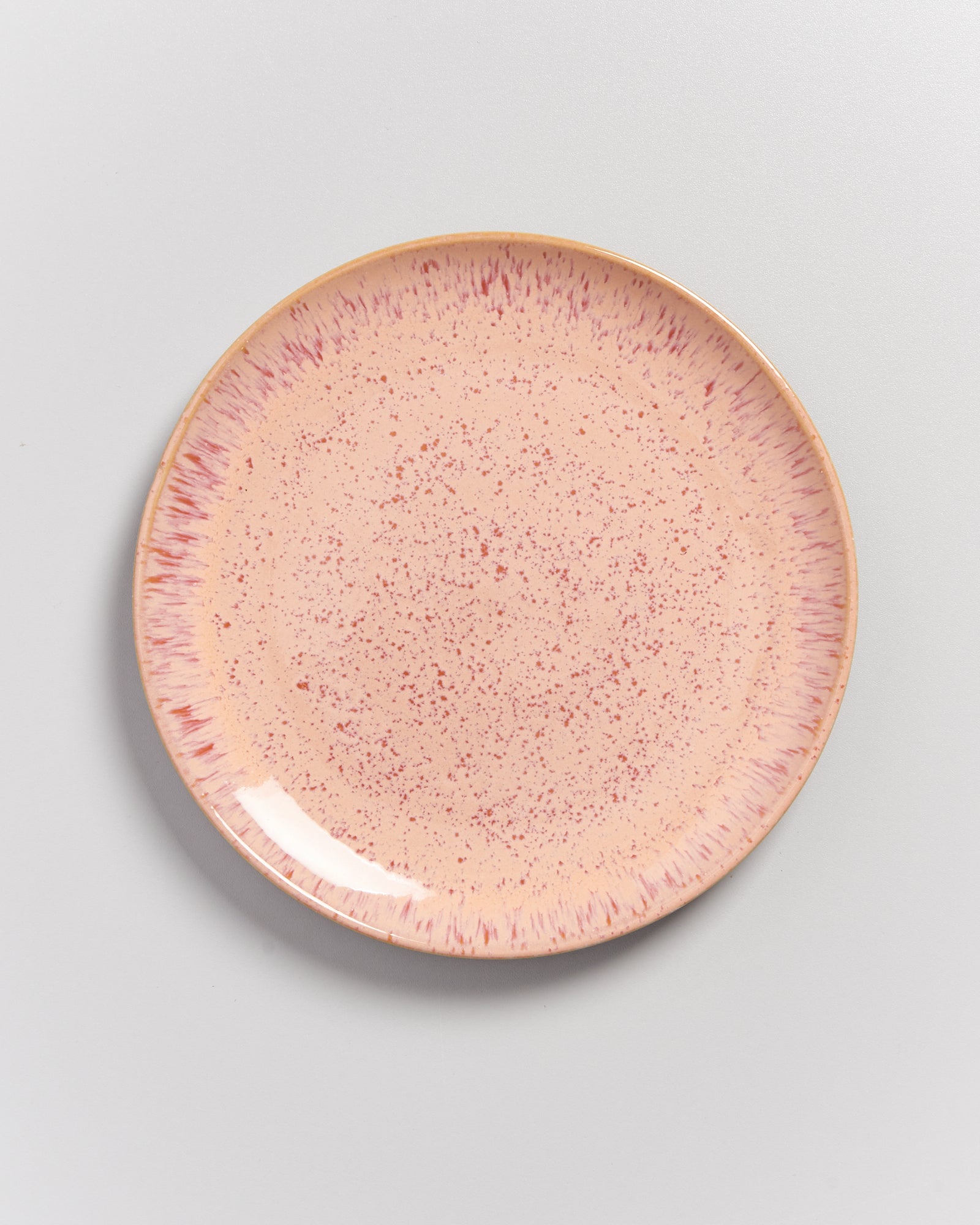 Runder Teller mit rosa Sprenkeln und Mustern auf cremefarbenem Hintergrund.