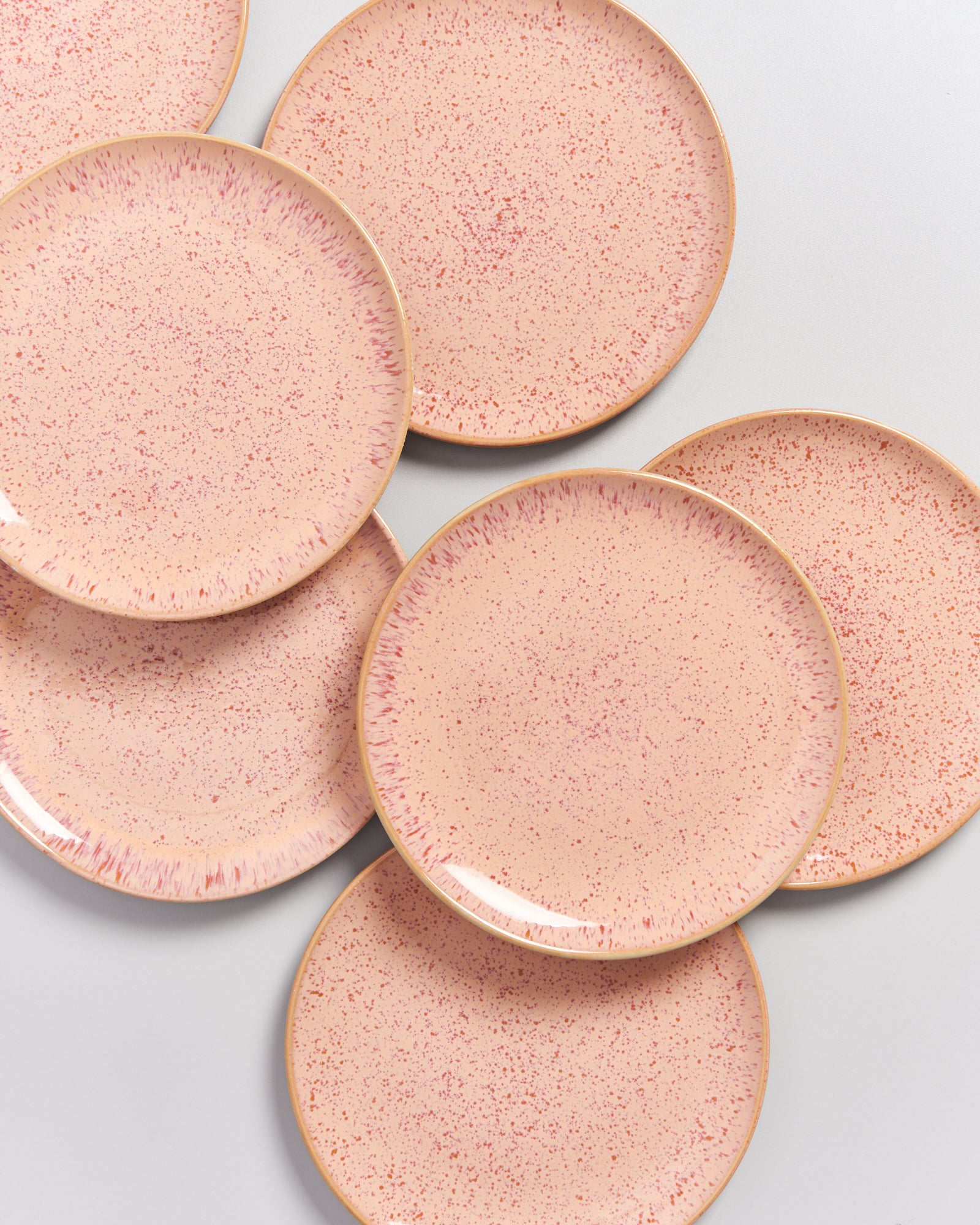 Mehrere rosafarbene Teller mit feinen Sprenkeln liegen überlappend auf einer weißen Oberfläche.