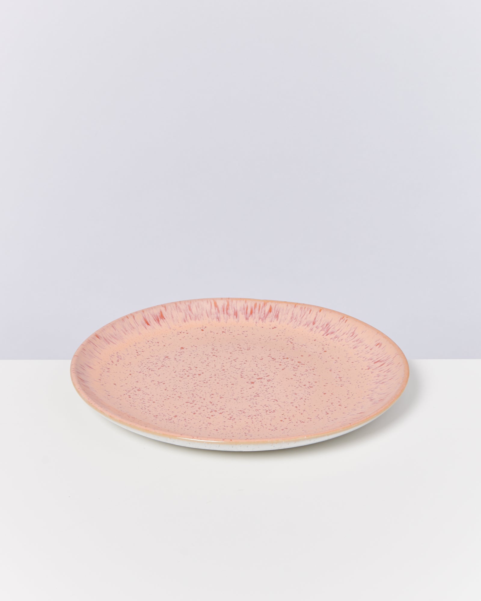Flacher, rosa Keramikteller mit gesprenkeltem Muster auf einer weißen Oberfläche.