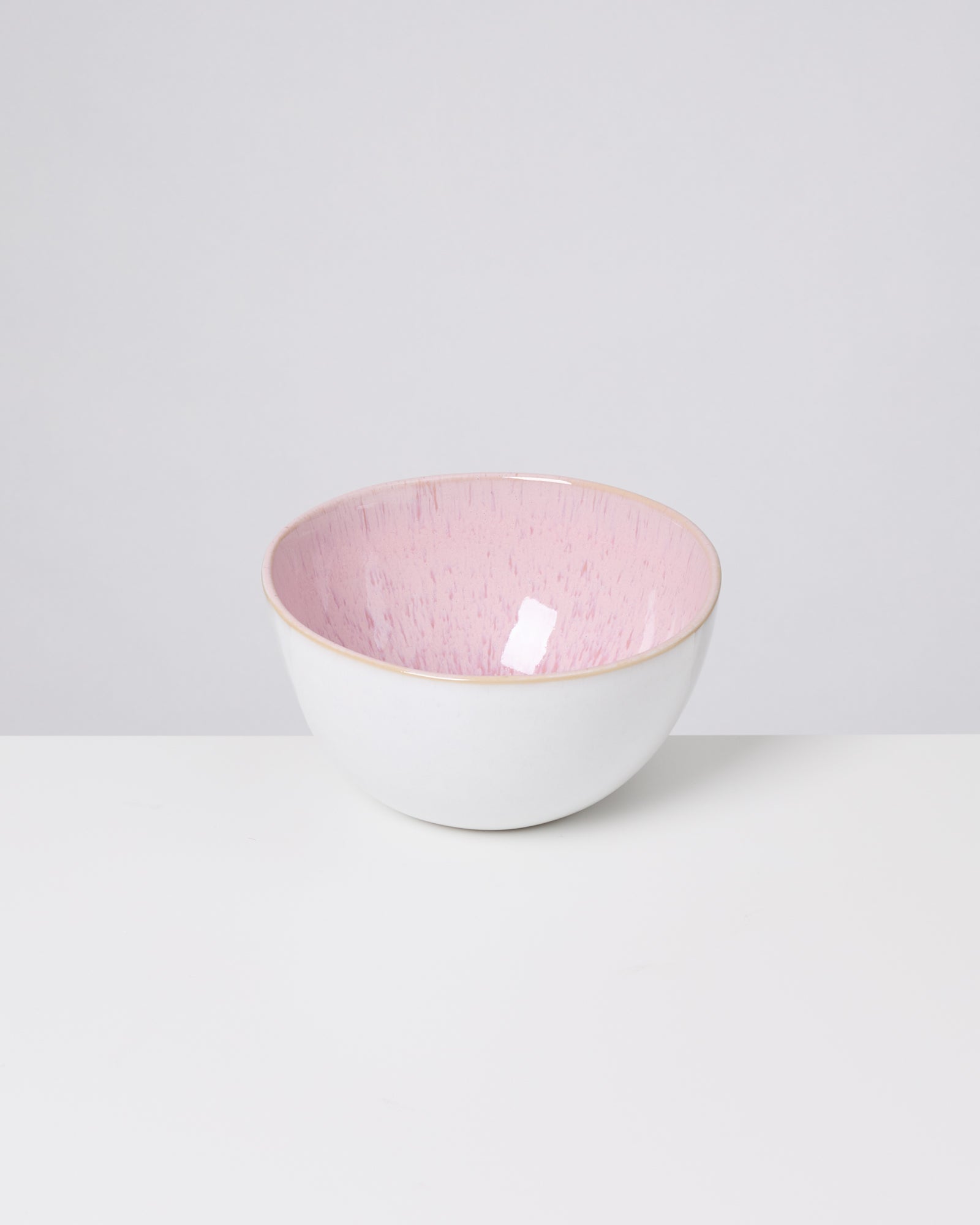 Weiße Schale mit rosa Innenfläche steht auf einem hellen, glatten Untergrund.