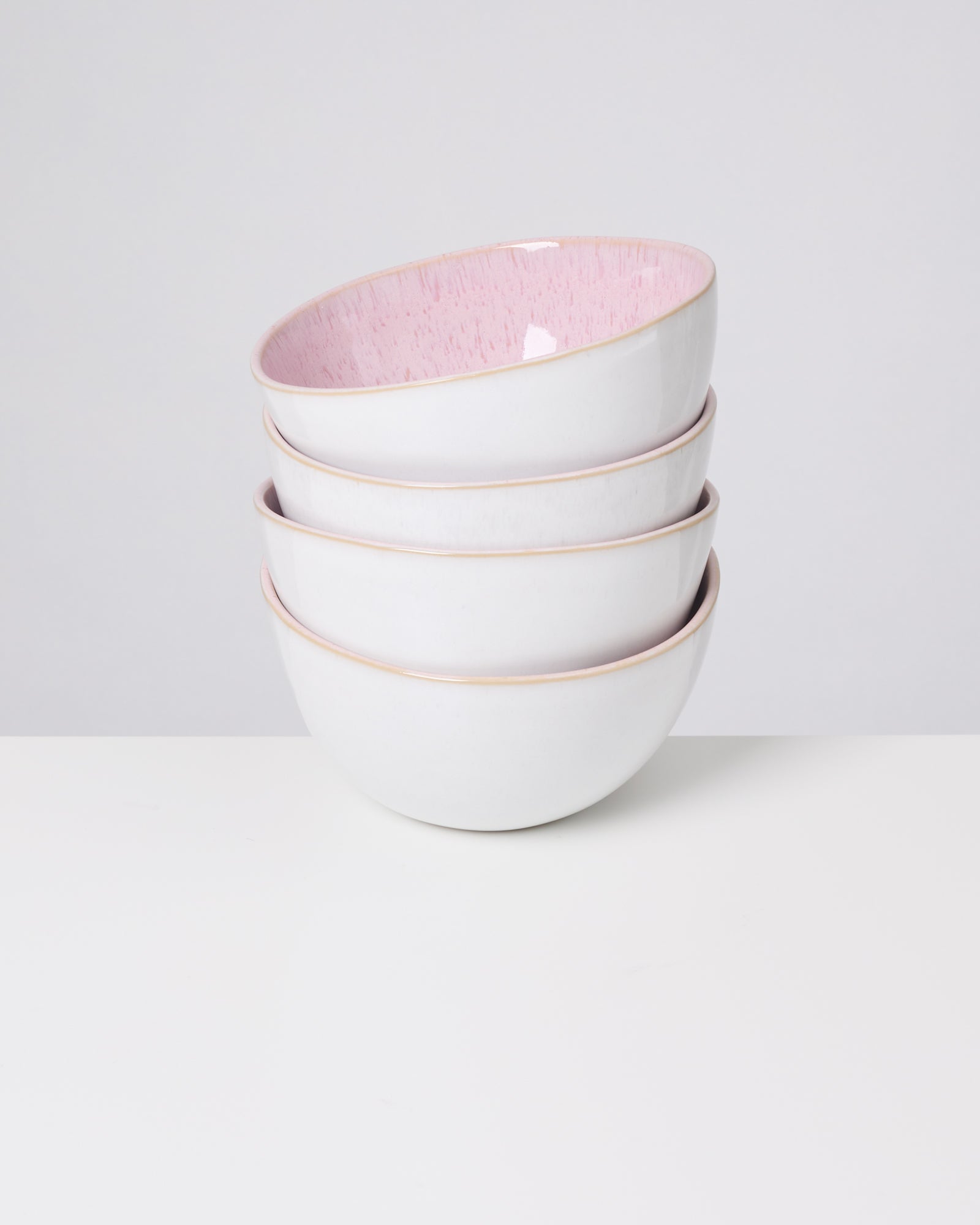 Vier übereinander gestapelte Schalen mit weißer Außenseite und rosa Innenseite auf einem weißen Hintergrund.