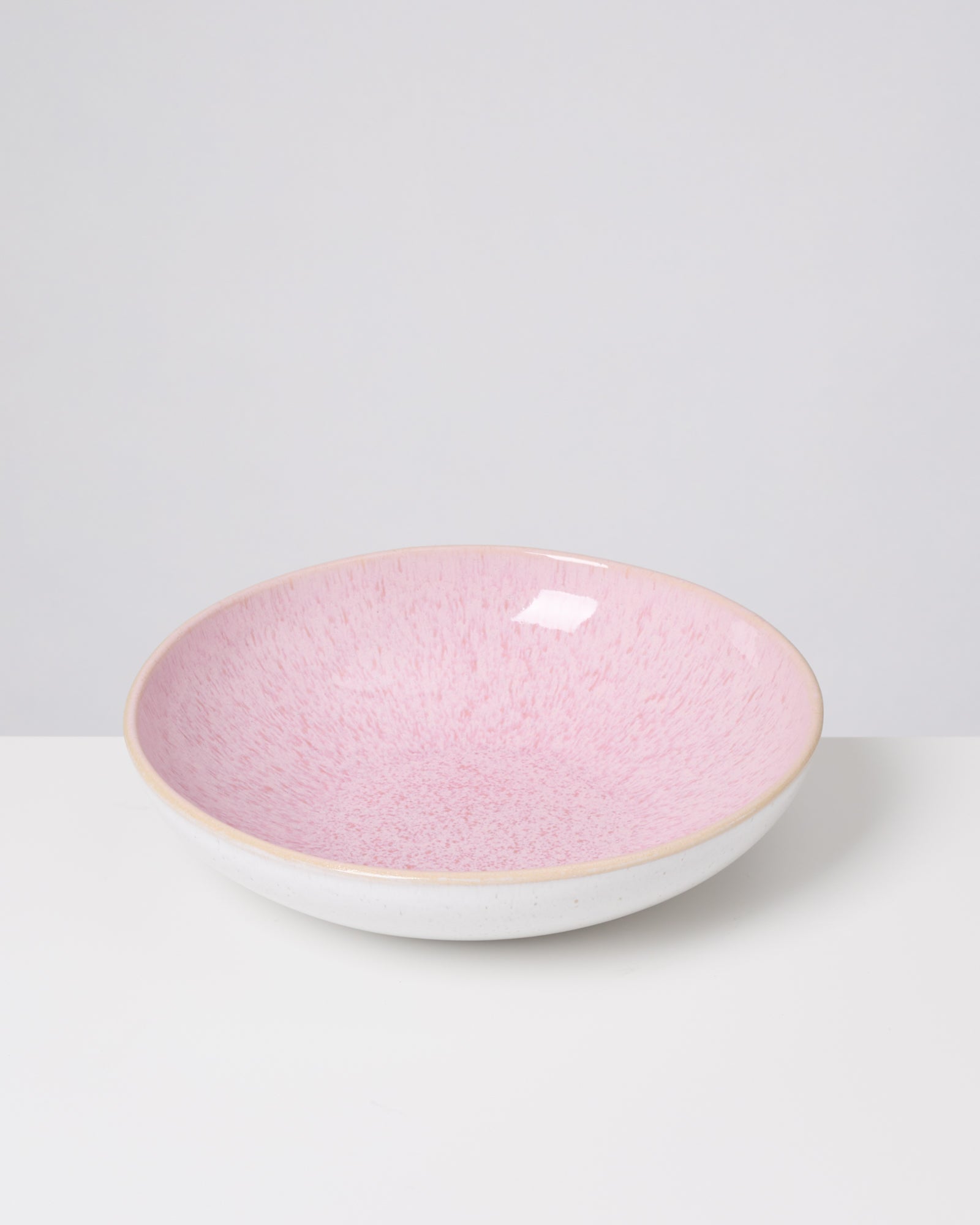 Runder, flacher Teller mit rosa Innenfläche und weißem Rand auf einem hellen Hintergrund.