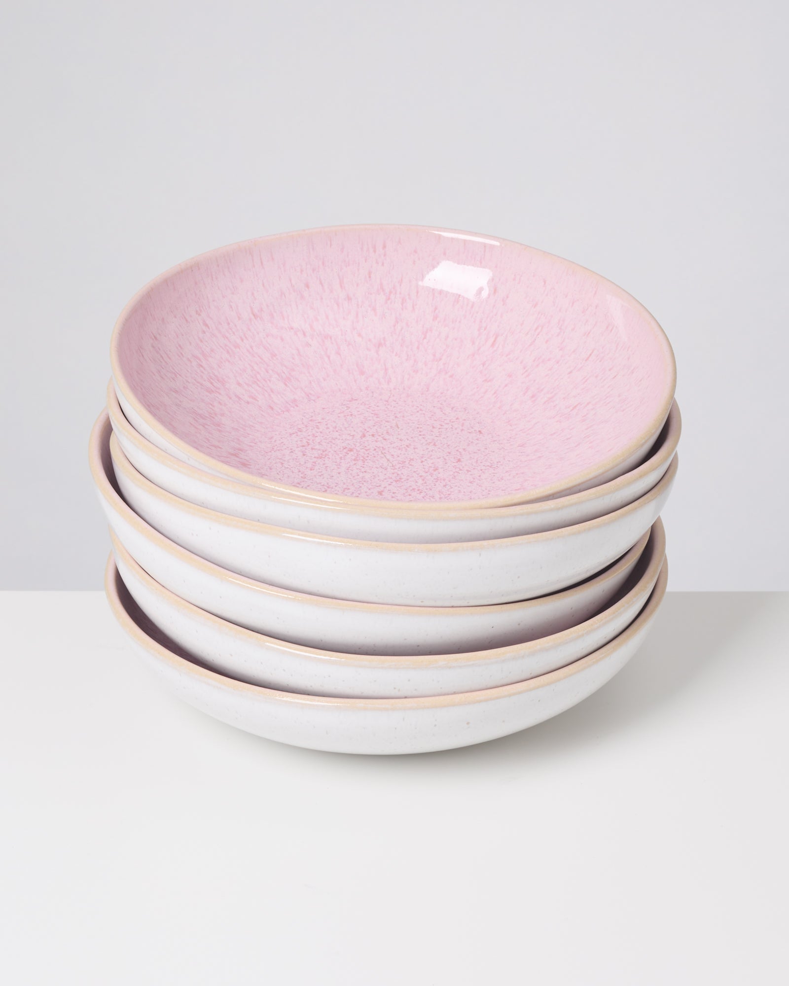 Vier gestapelte Schalen mit weißer Außenseite und rosa Innenseite auf einem Tisch.