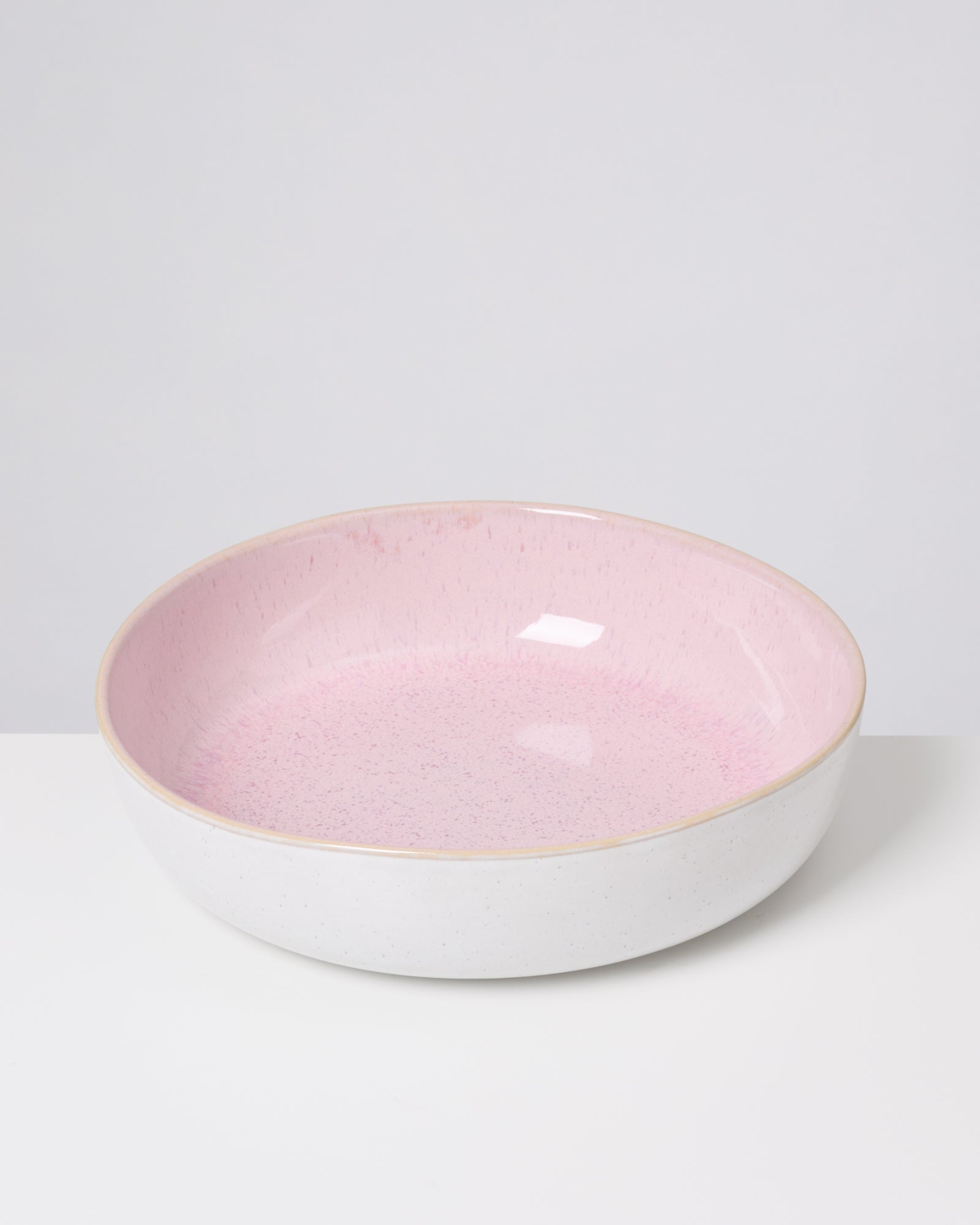 Eine flache Schüssel mit rosa Innenfläche und weißer Außenseite auf einem weißen Hintergrund.