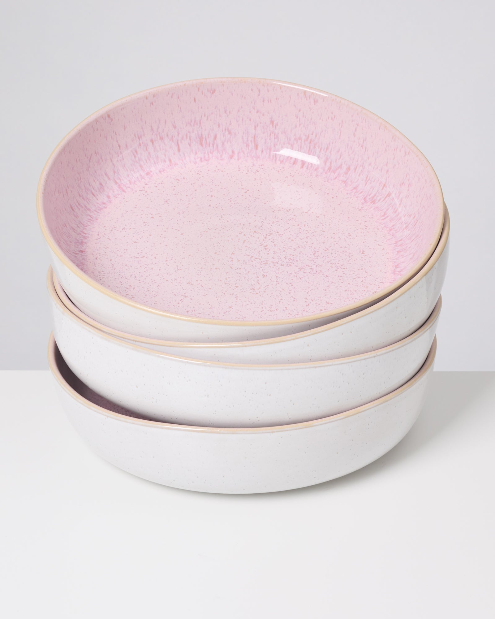 Vier gestapelte Keramikteller mit rosa Innenseite und weißem Äußeren auf weißem Hintergrund.