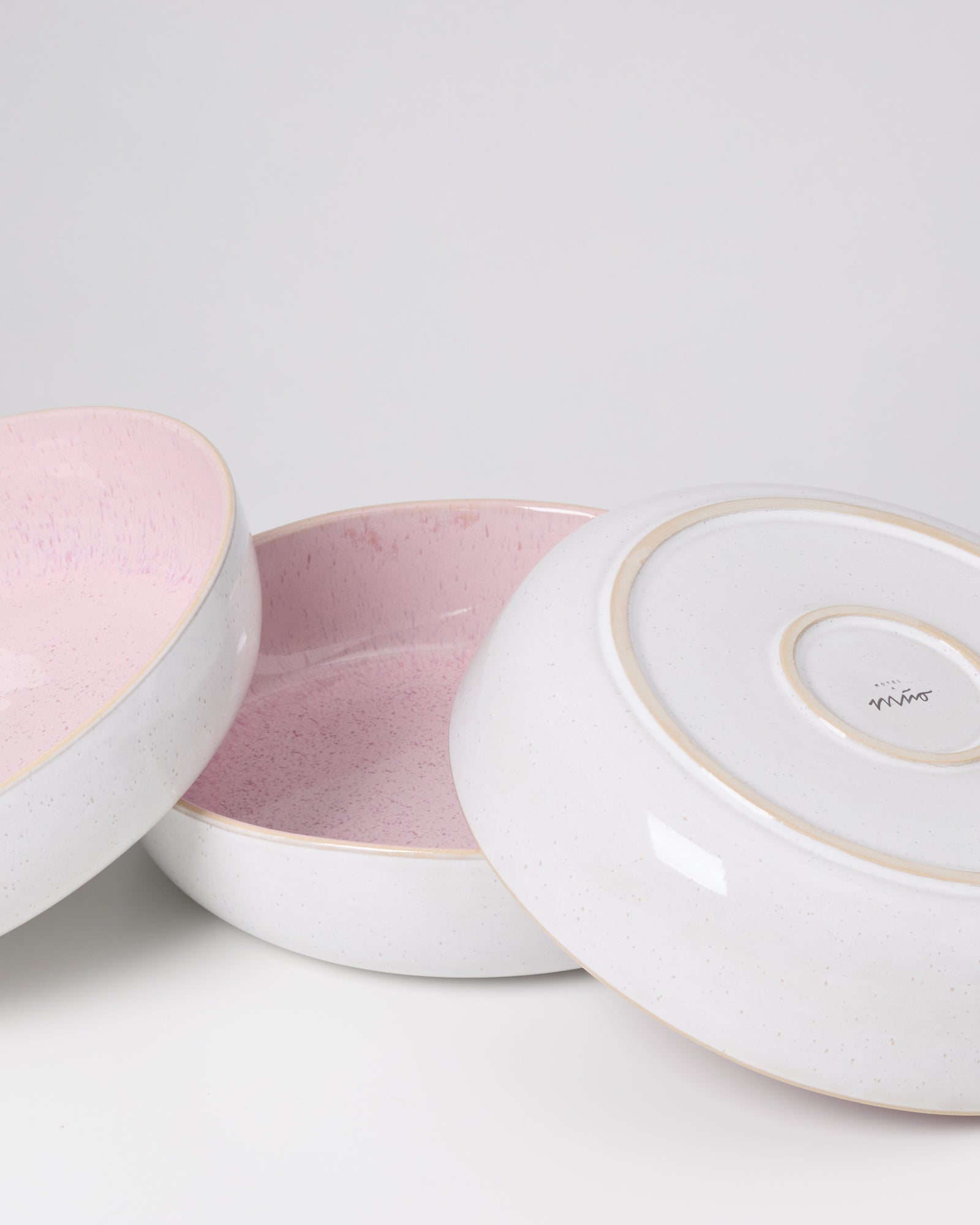 Drei runde Keramikschalen mit rosa Innenflächen, eine ist umgedreht, auf weißem Hintergrund.