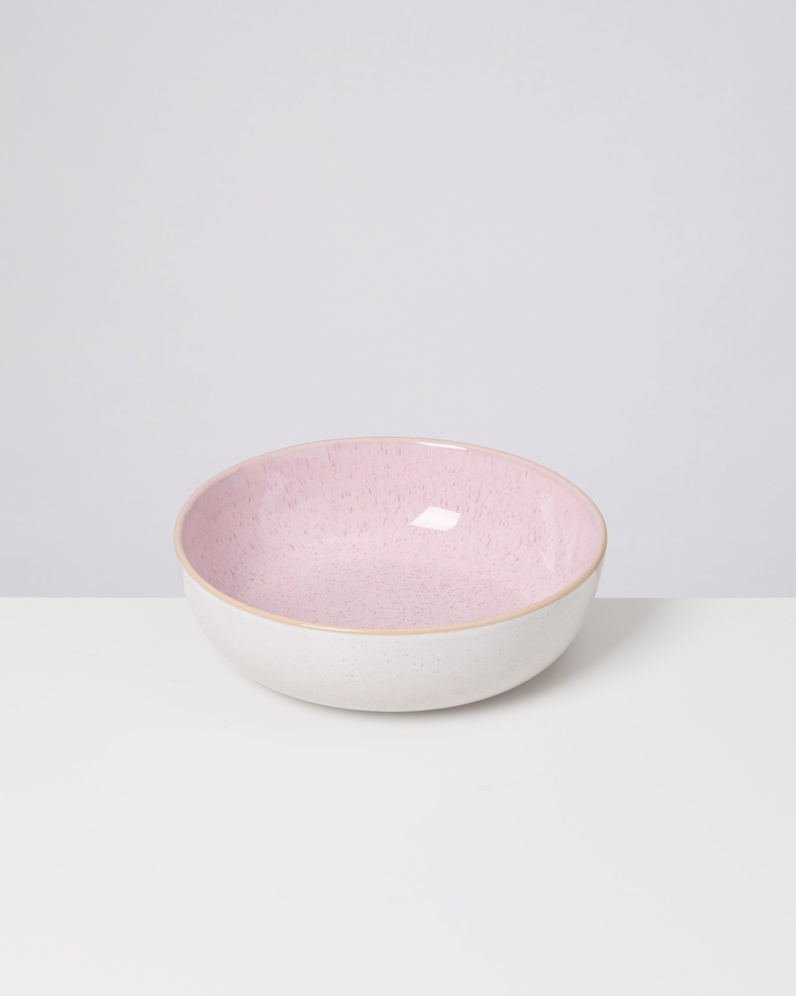 Weiße Schale mit rosa Innenfläche steht auf einem weißen Tisch vor grauem Hintergrund.