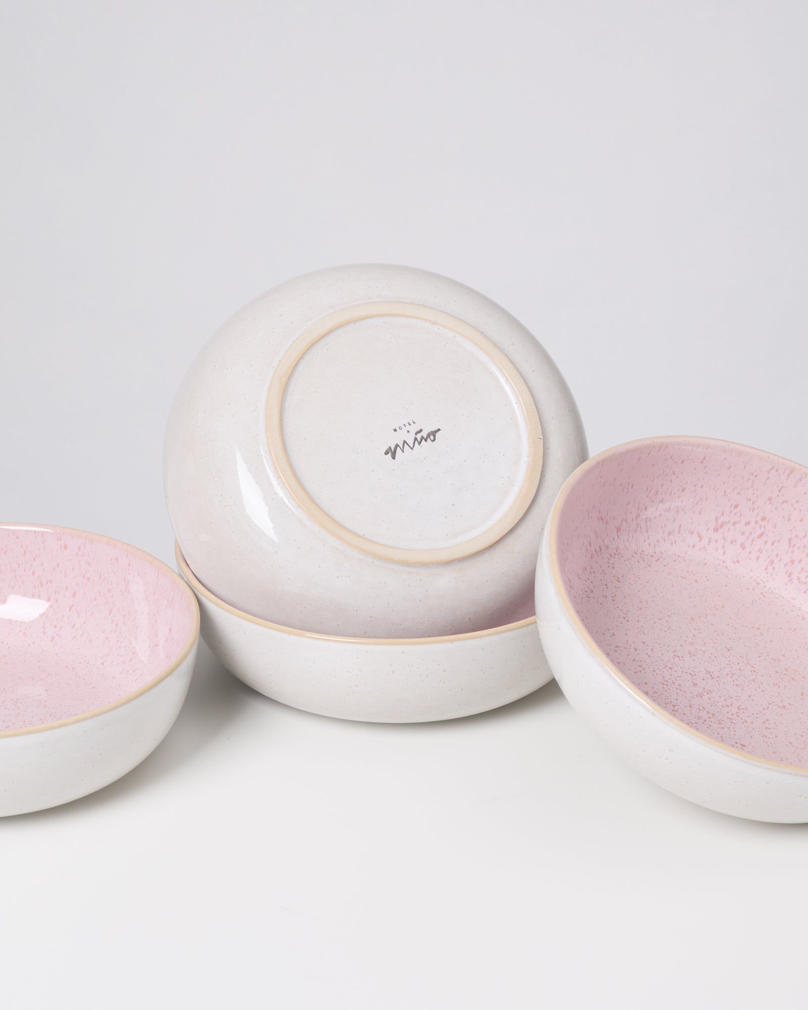 Vier Keramikschalen mit weißer Außenseite und rosa Innenseite, eine Schale zeigt den gestempelten Boden.