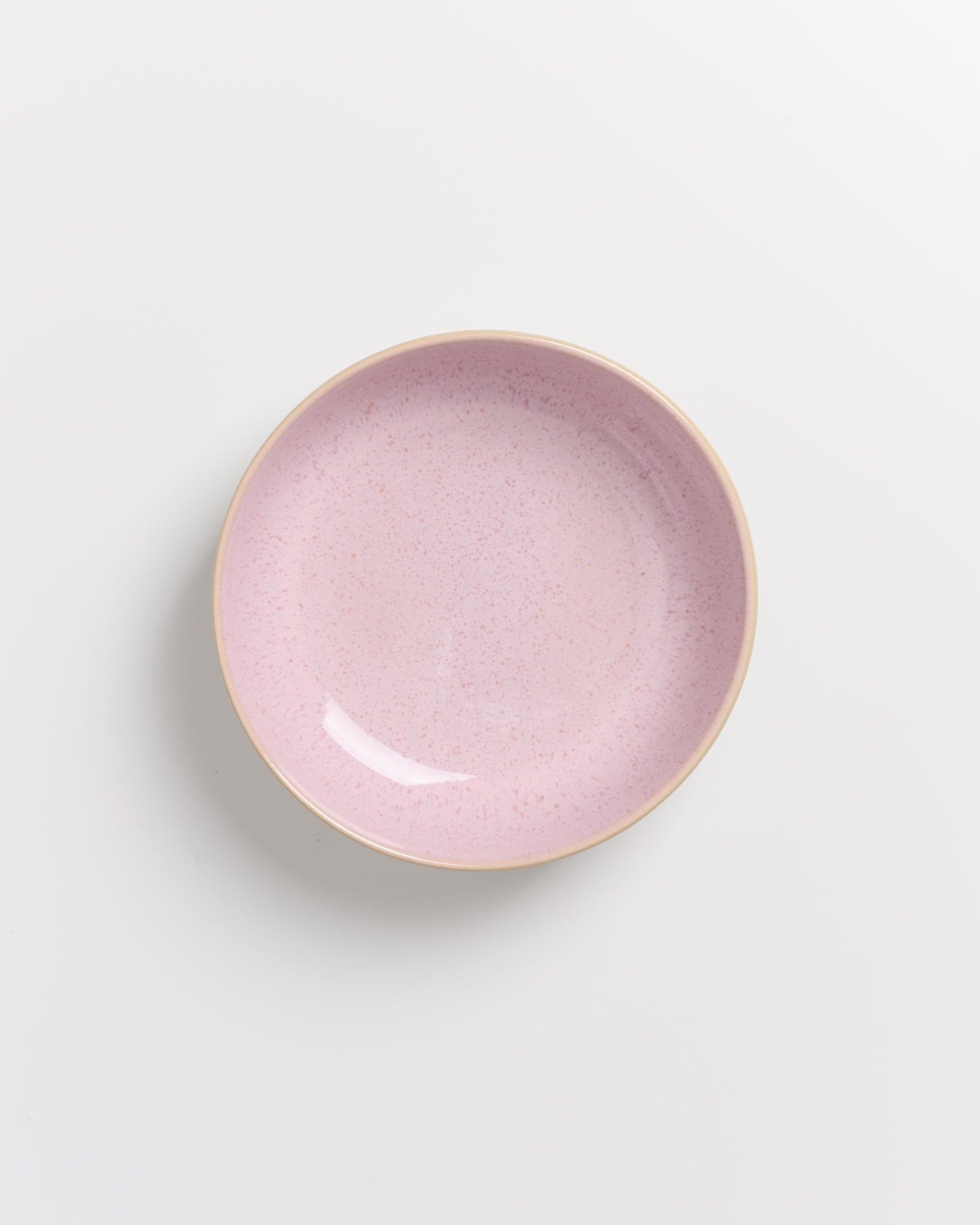 Ein rosafarbener Teller mit einem cremigen Rand auf weißem Hintergrund.