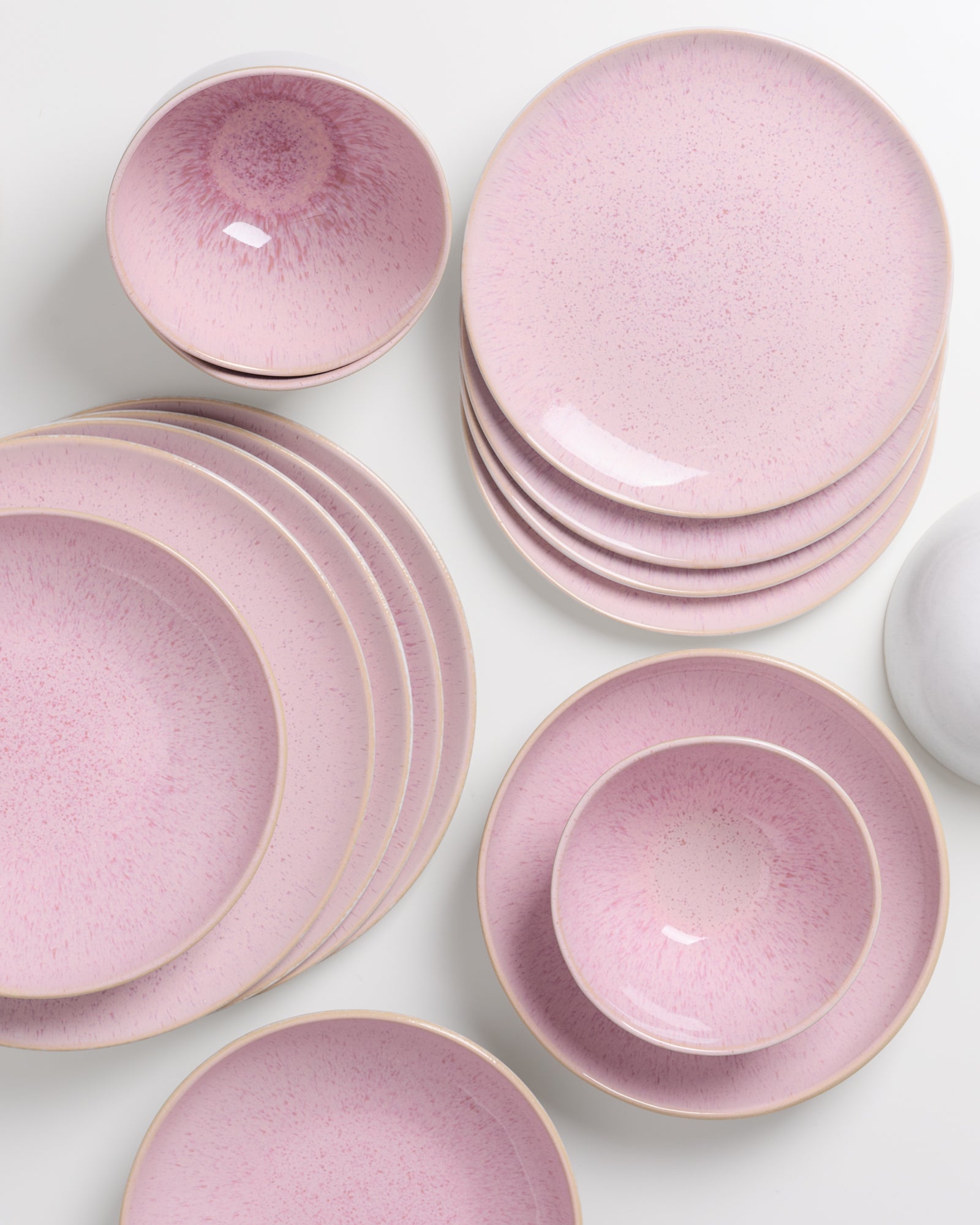 Rosafarbene Keramikgeschirrsets mit Tellern und Schalen auf weißem Hintergrund.