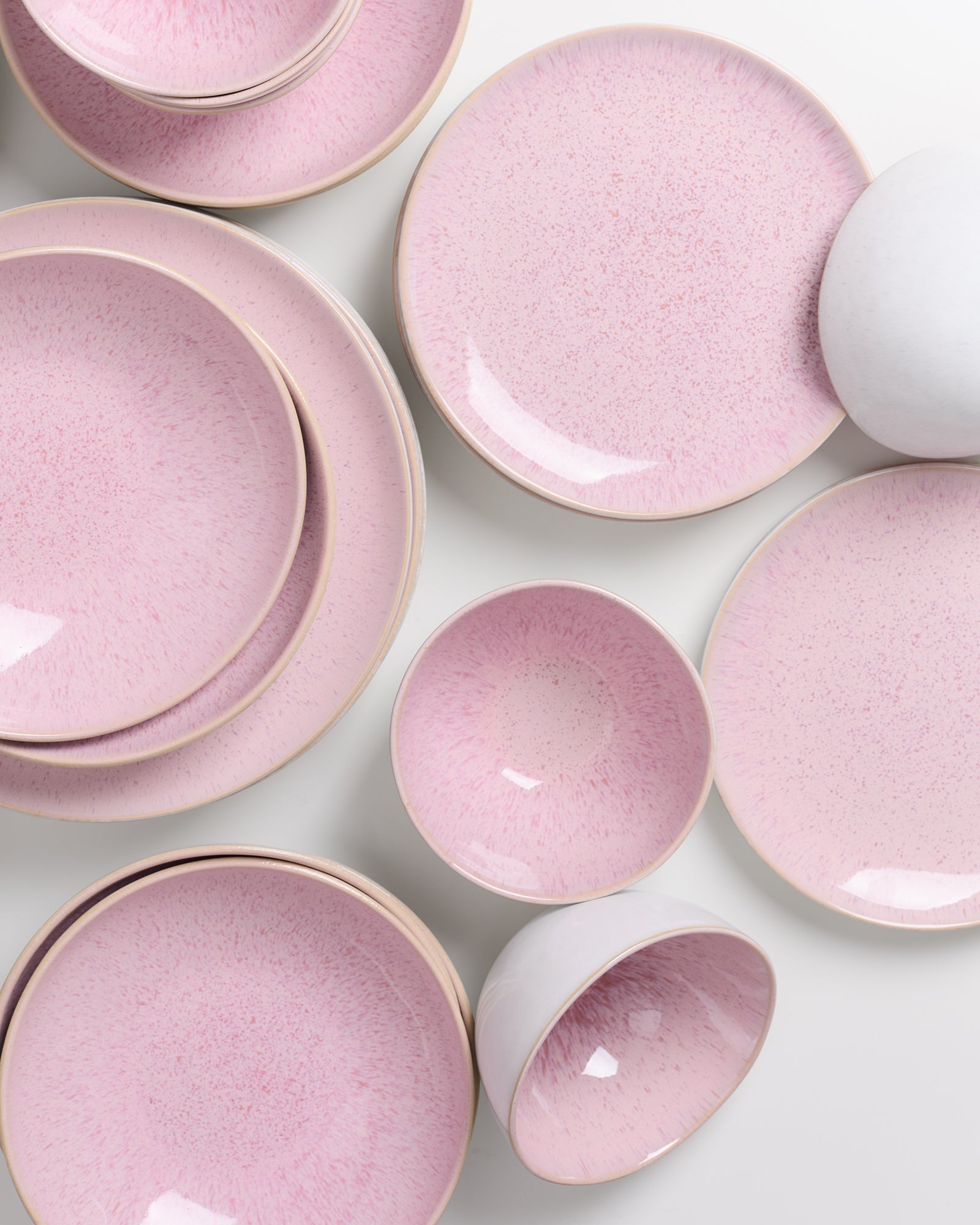 Mehrere rosafarbene Teller und Schüsseln mit zart gesprenkelten Mustern liegen auf einer weißen Oberfläche.