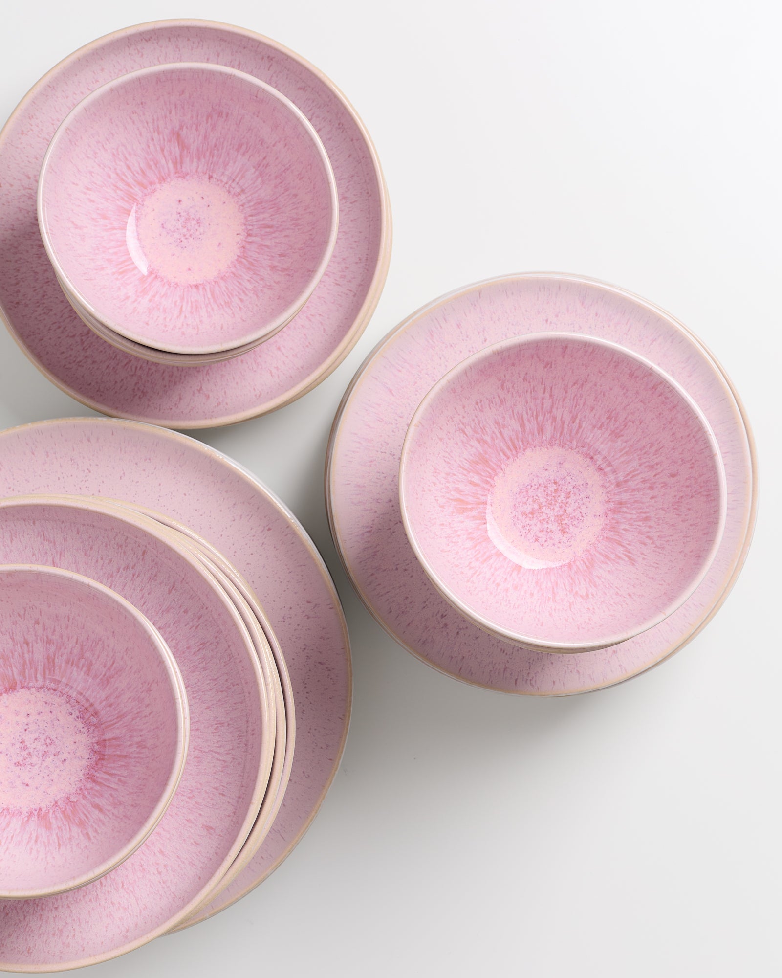 Ein Set aus rosa Keramiktellern und -schalen mit gesprenkeltem Muster auf einem weißen Hintergrund.