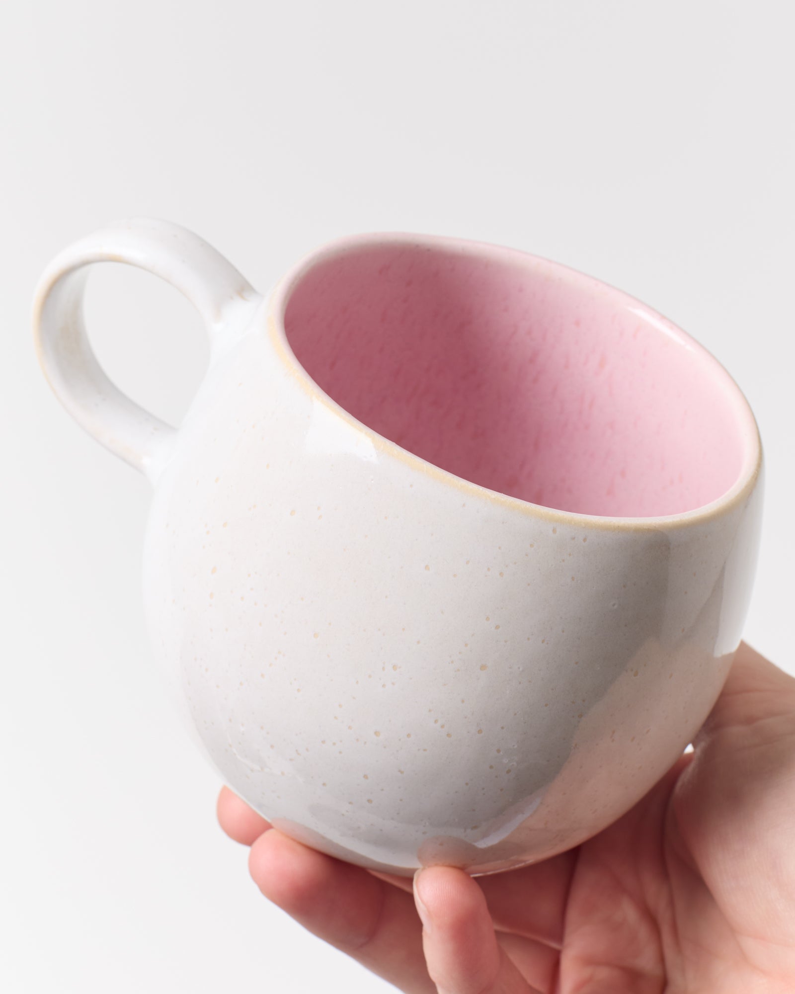 Eine Hand hält eine weiße Tasse mit rosa Innenseite vor einem hellen Hintergrund.