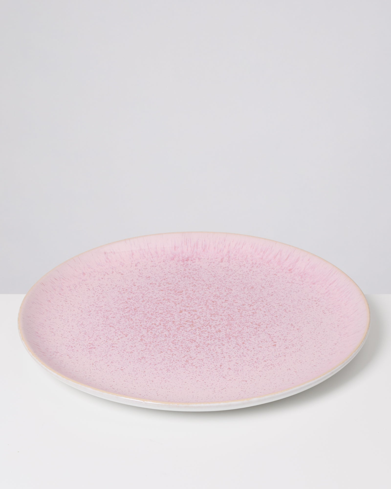 Ein rosafarbener Teller mit gesprenkeltem Muster steht auf einer weißen Oberfläche vor einem neutralen Hintergrund.