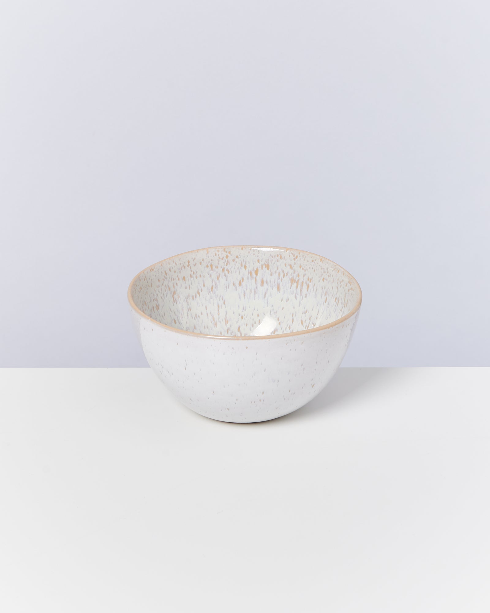 Weiße Keramikschüssel mit gesprenkeltem Muster auf weißem Untergrund vor einer hellgrauen Wand.