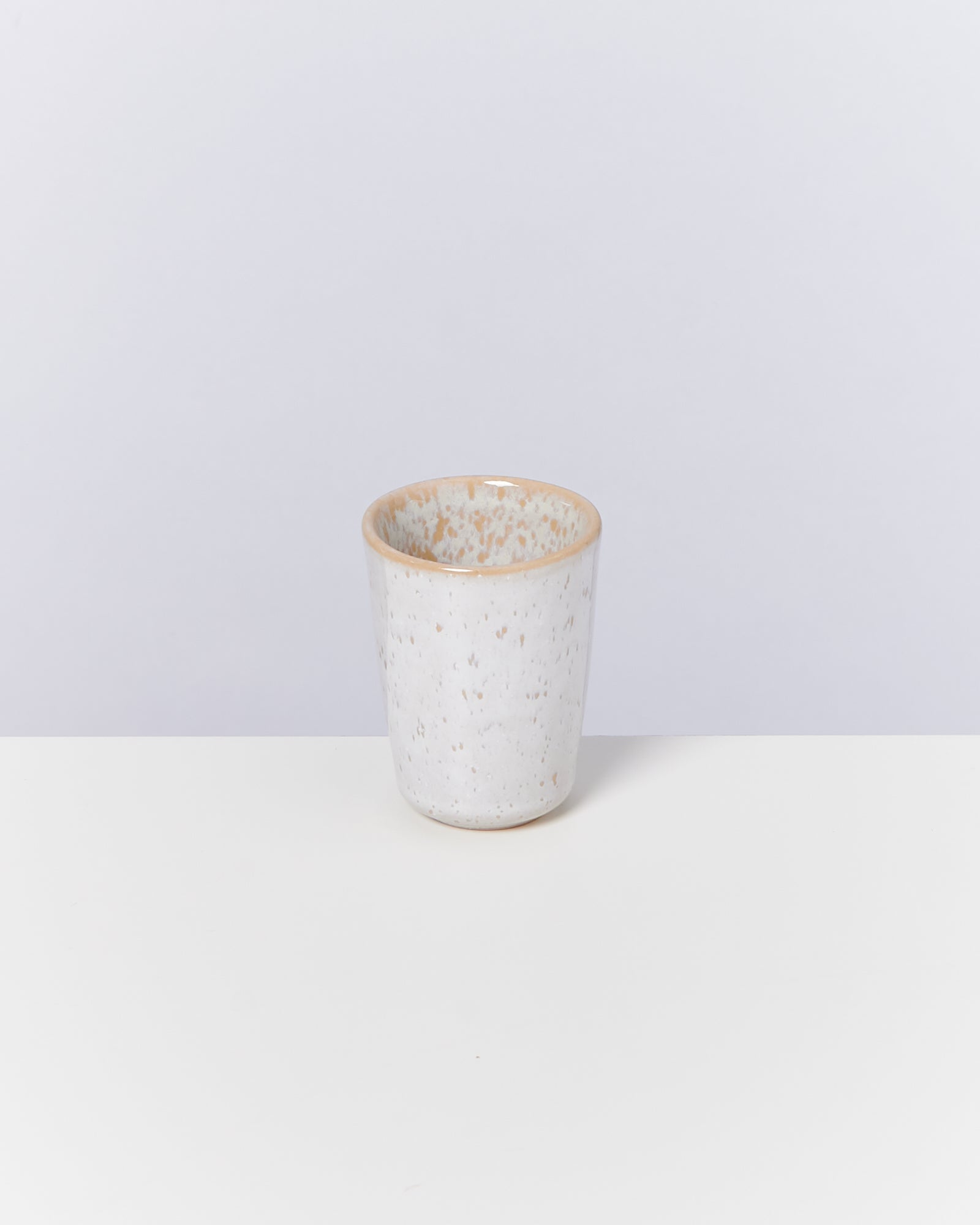 Weiße, gesprenkelte Keramiktasse auf einem Tisch vor neutralem Hintergrund.