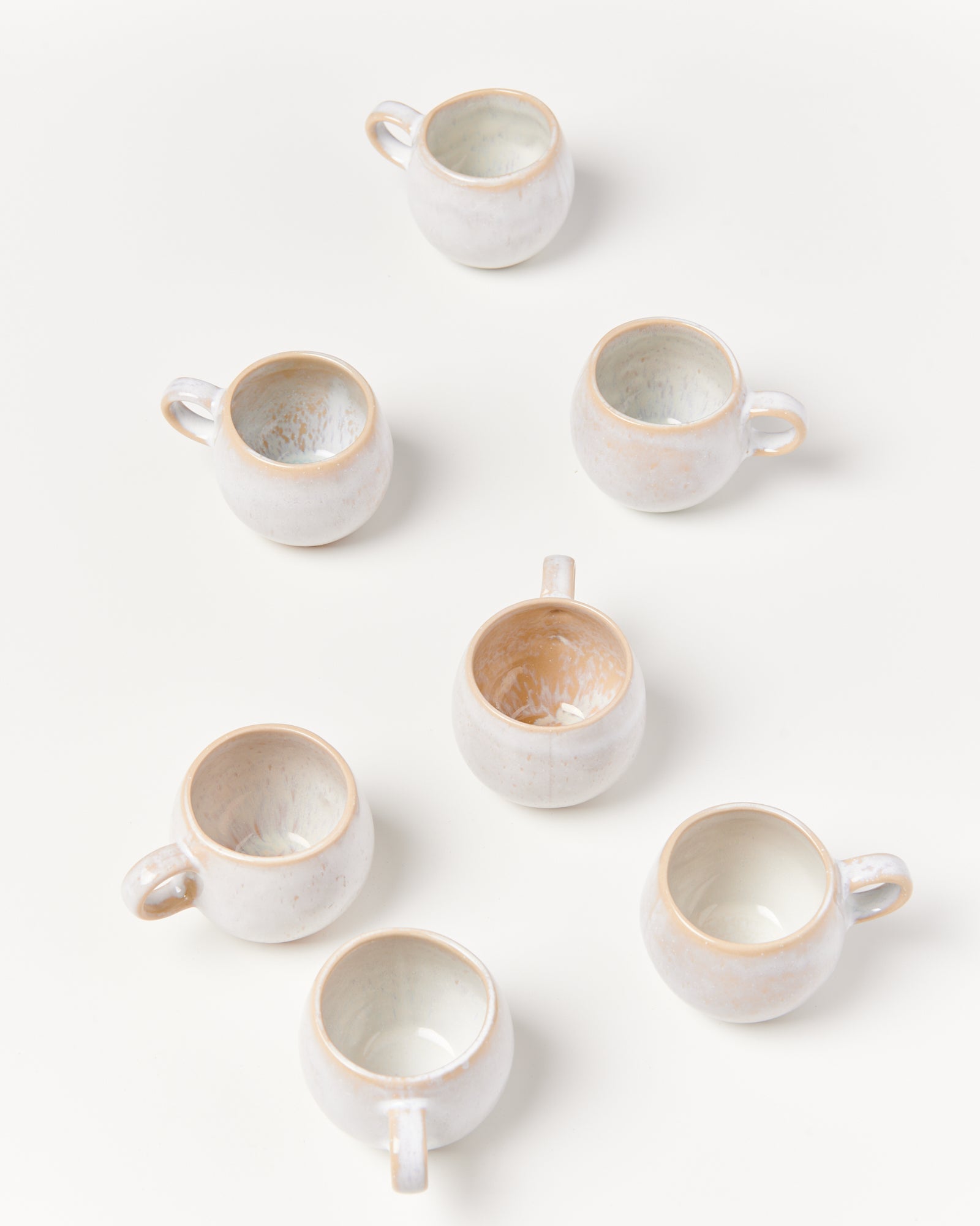 Sieben weiße Keramiktassen, von oben betrachtet, auf weißem Hintergrund arrangiert.