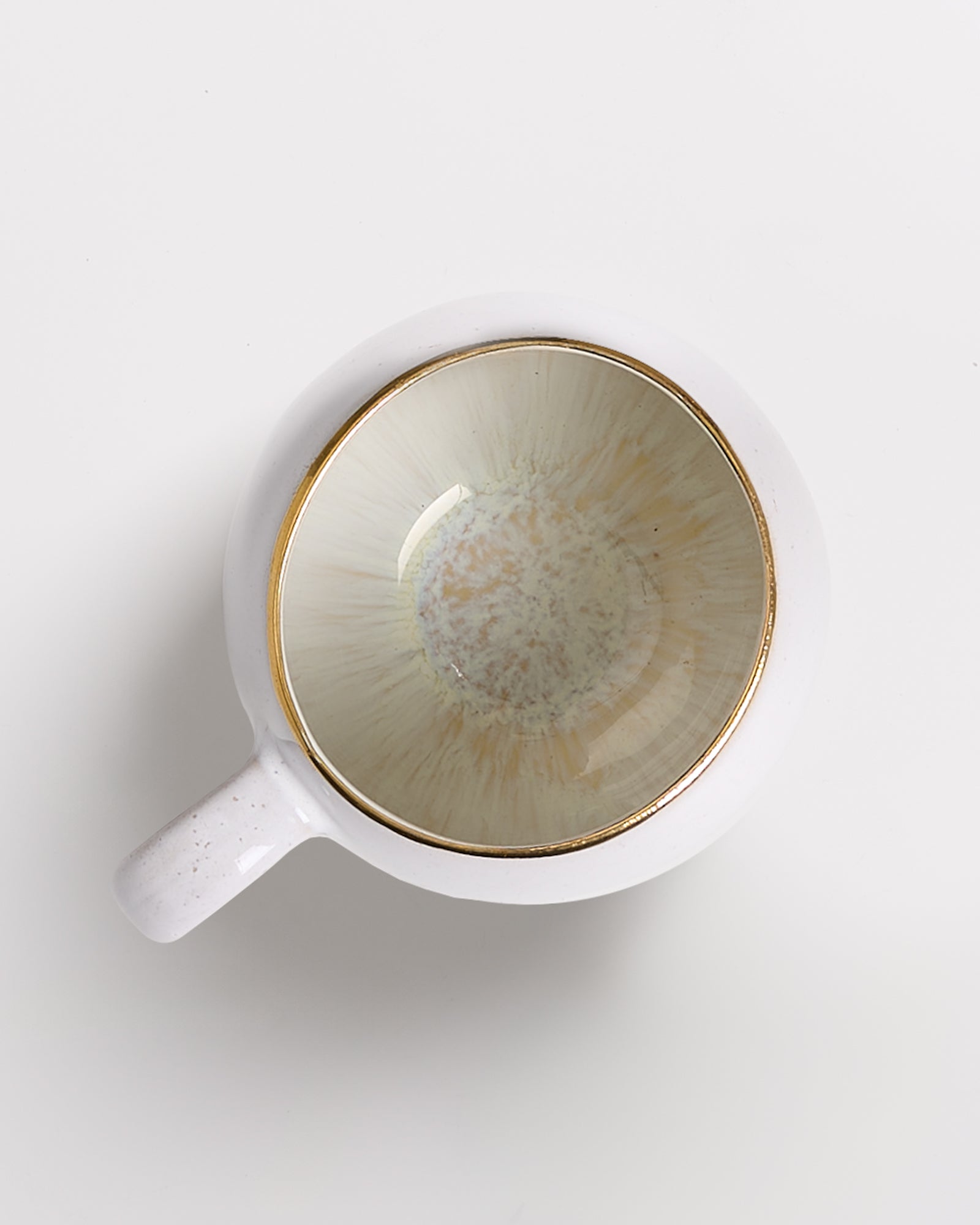 Weiße Tasse mit grünlichem Innenmuster und goldener Kante auf weißem Hintergrund, von oben fotografiert.