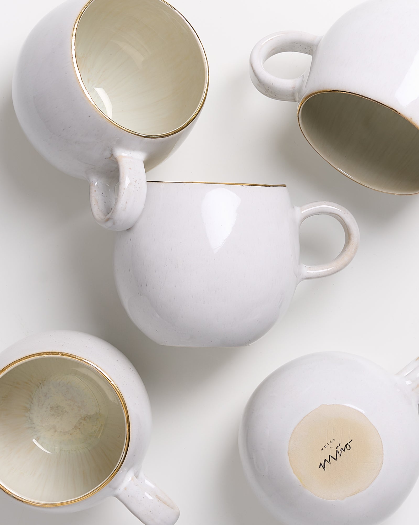 Fünf weiße Keramiktassen mit goldenen Rändern sind auf einem weißen Hintergrund angeordnet.
