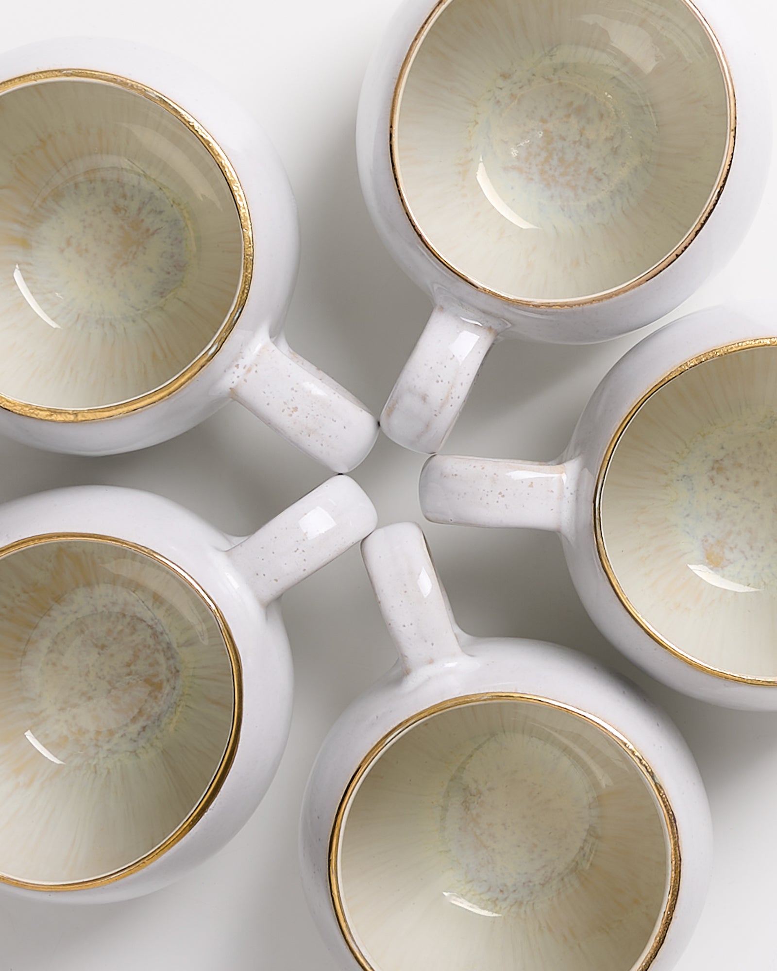 Fünf weiße Tassen mit goldenen Rändern im Kreis angeordnet, von oben betrachtet.