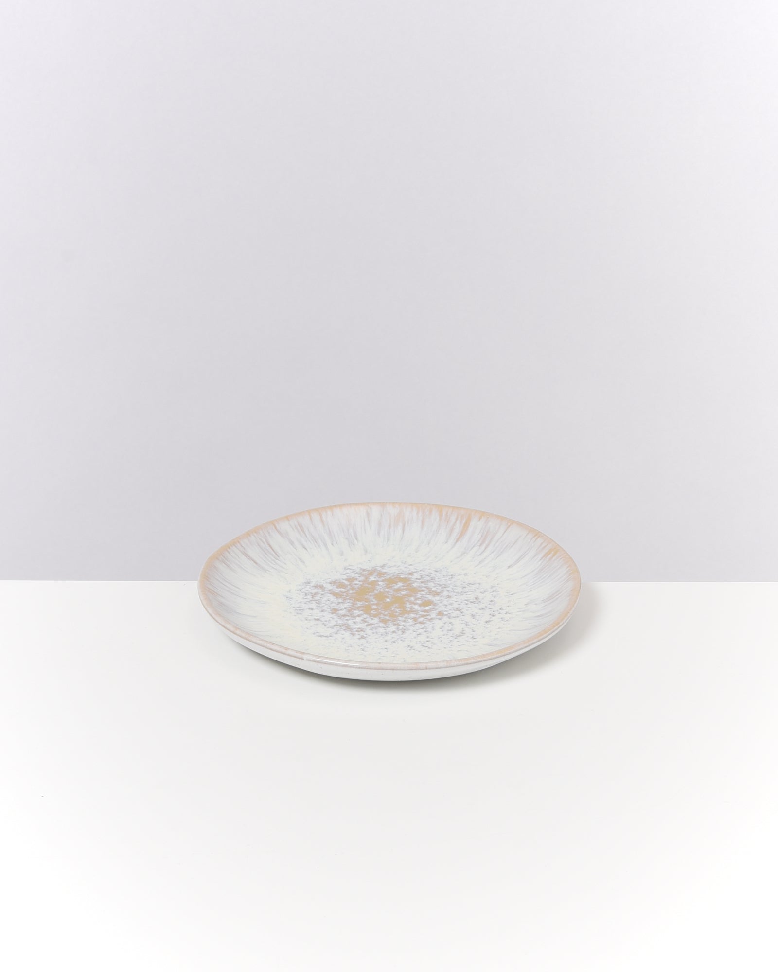 Keramikteller mit zartem Muster aus blauen und braunen Sprenkeln auf einem weißen Hintergrund.