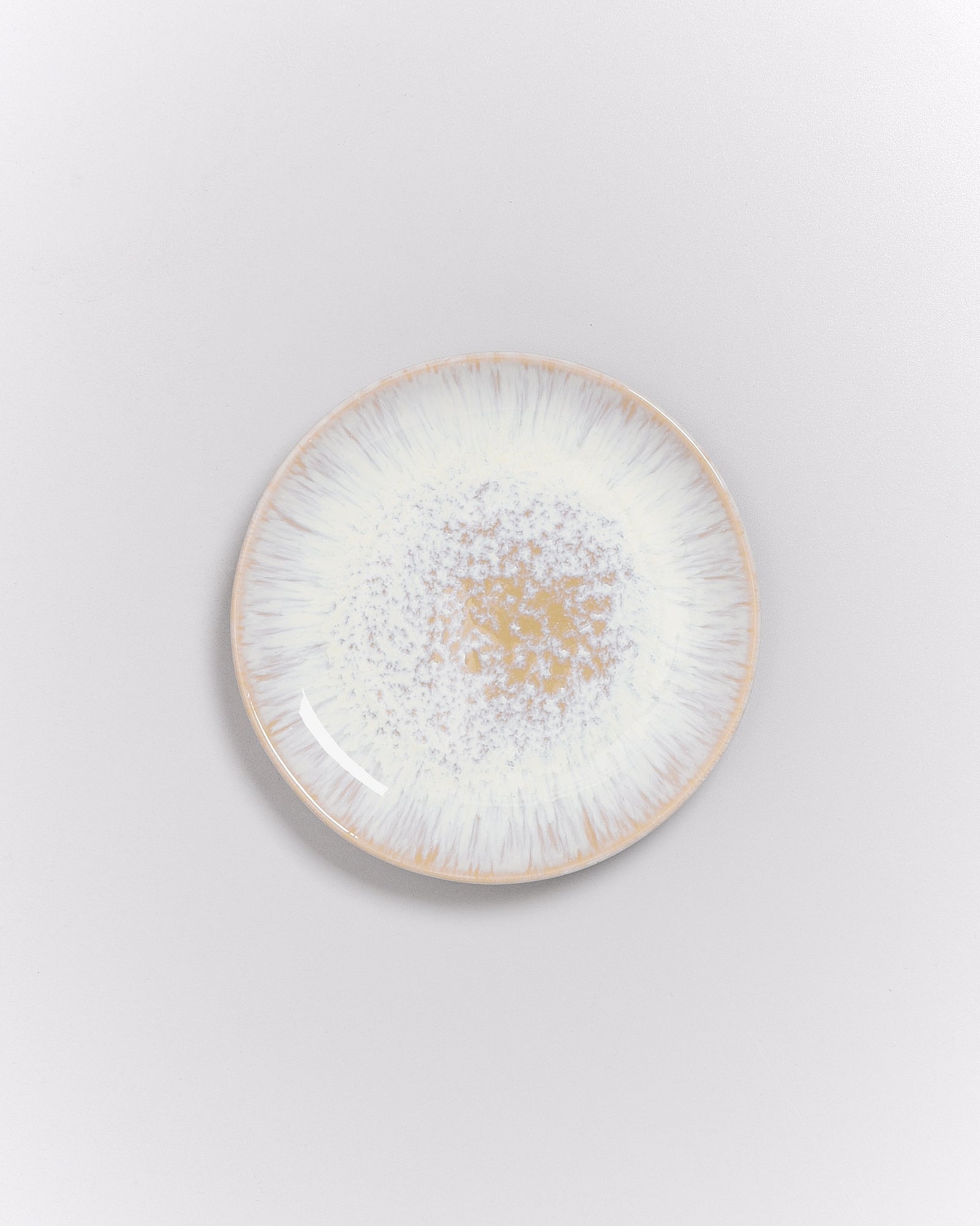 Runde Keramikplatte mit einem weißen und braunen, gesprenkelten Muster auf einem hellen Hintergrund.