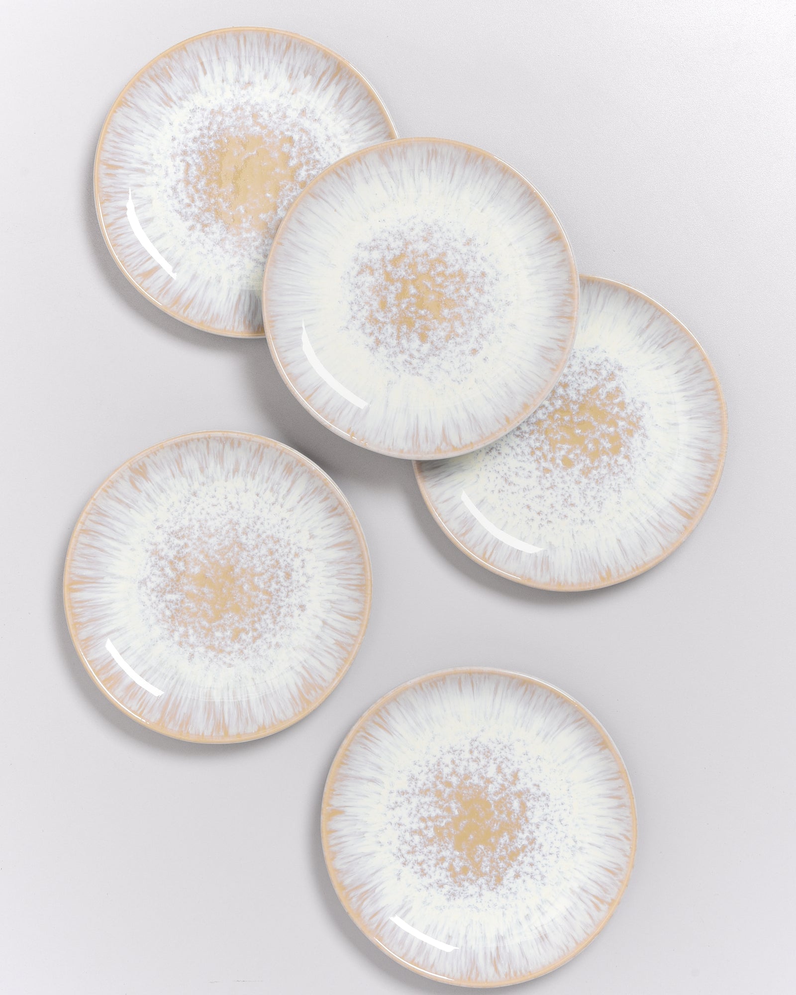 Fünf runde Teller mit beigefarbenem und weißem Muster, auf einer hellgrauen Oberfläche arrangiert.