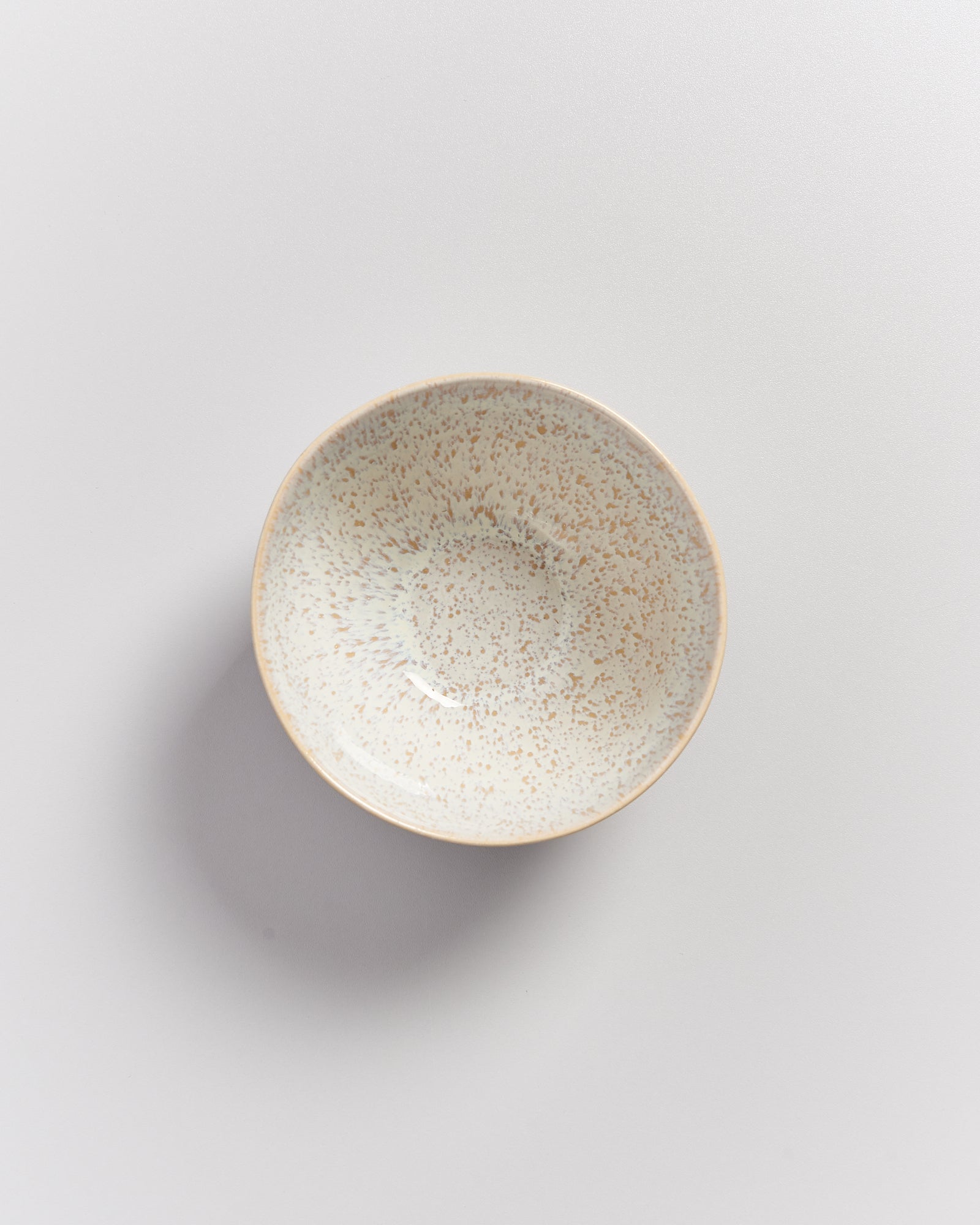 Eine beige, gesprenkelte Schale auf einer weißen Oberfläche.