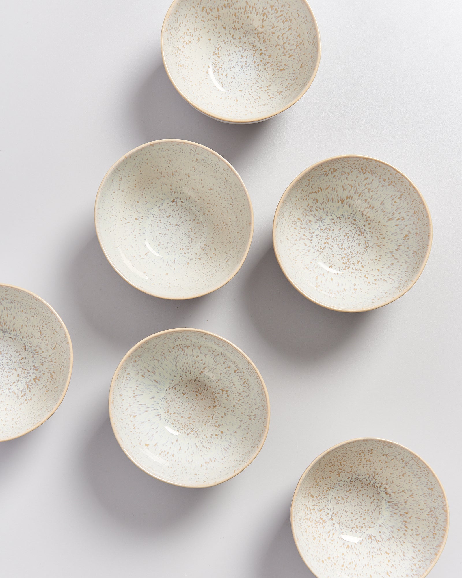 Sechs beige, gesprenkelte Schalen auf weißem Hintergrund, geometrisch angeordnet.