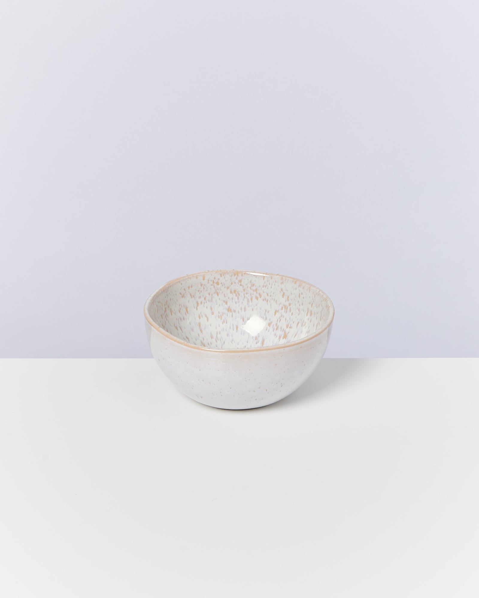 Handgefertigte, gesprenkelte Keramikschale auf einem weißen Tisch vor einem hellgrauen Hintergrund.