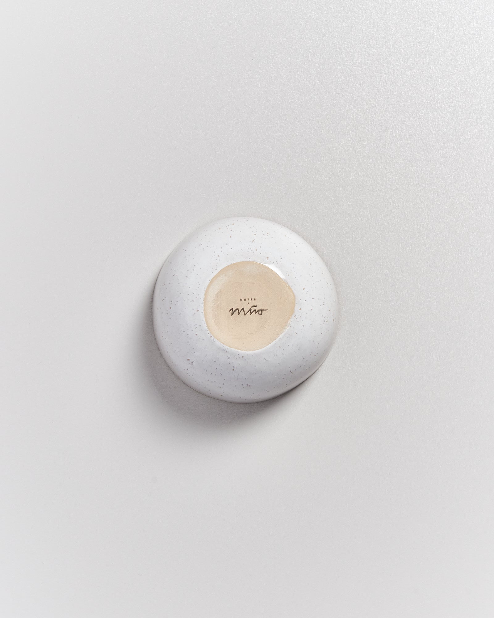 Weiße, runde, glatte Seifenschale auf hellem Hintergrund, mit einem hellen Kreis in der Mitte und Schriftzug darin.