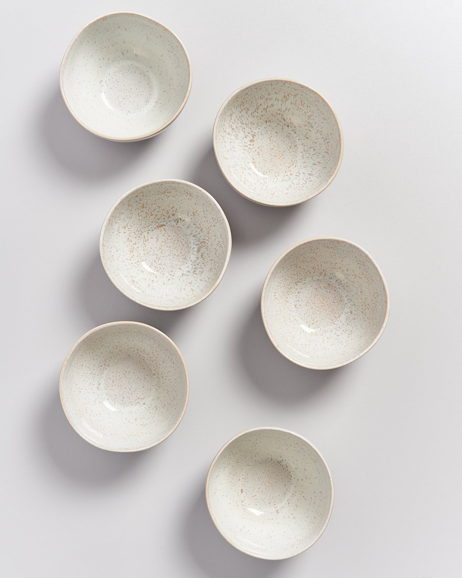 Sechs weiße Schalen mit braunen Sprenkeln, symmetrisch auf einer hellen Oberfläche angeordnet.