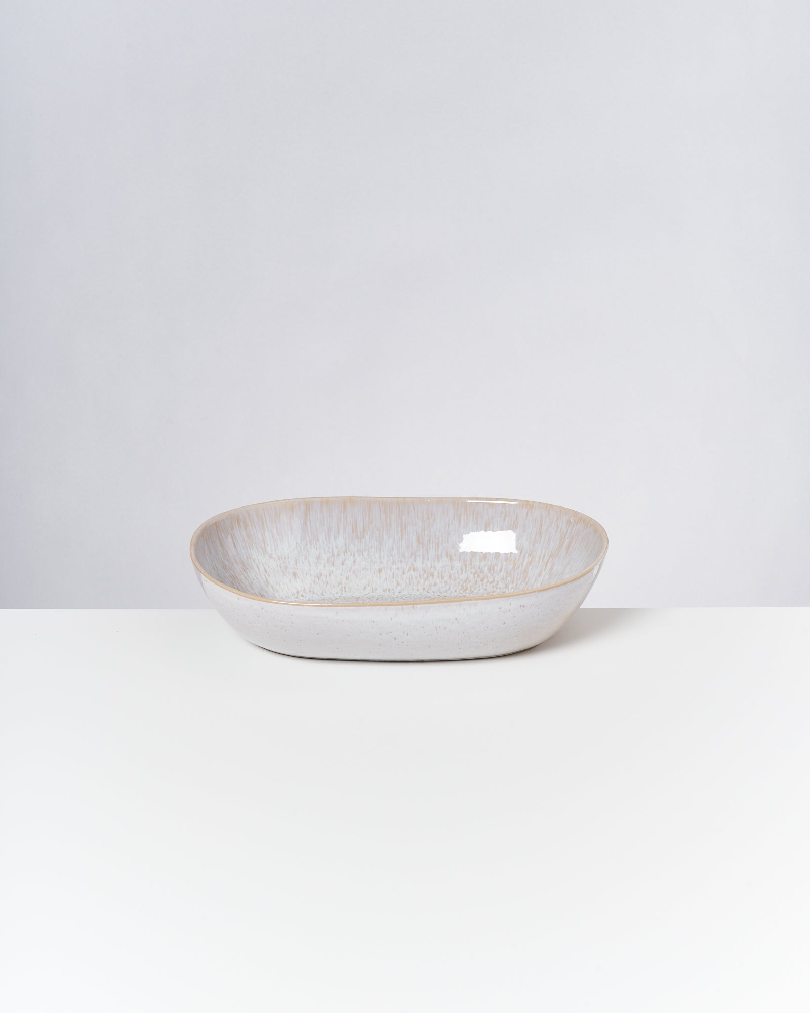 Ein ovaler, hellgrauer Keramikteller mit dezentem Muster steht auf einem weißen Untergrund.