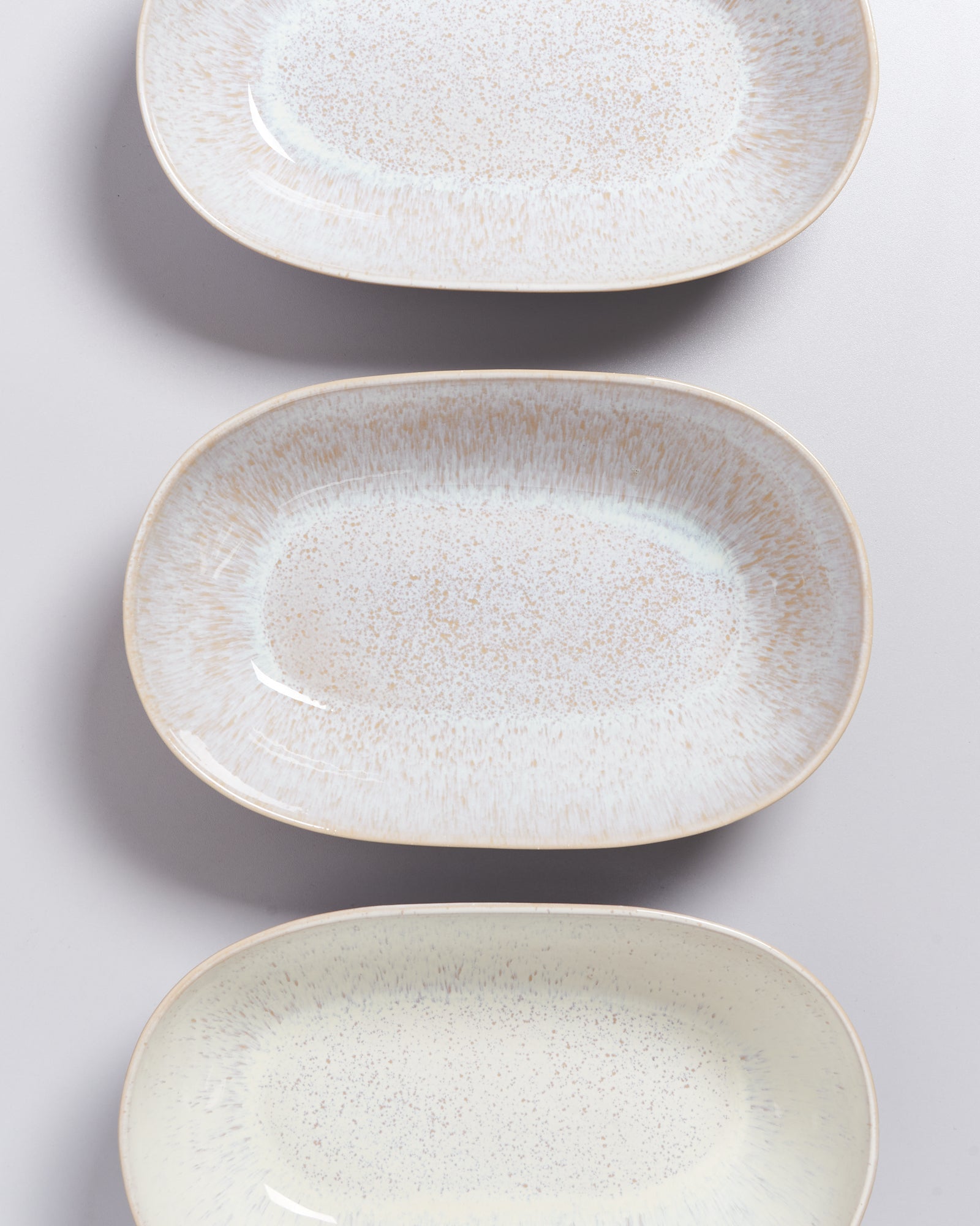 Drei rechteckige, beige-gesprenkelte Teller in einer vertikalen Anordnung auf einer grauen Oberfläche.