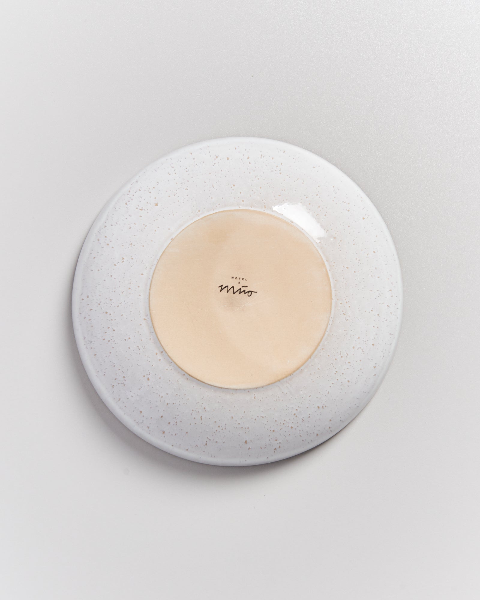 Rückseite eines Tellers mit Aufschrift "Hotel Miro", umgeben von hellem Rand mit Sprenkeln auf grauem Hintergrund.